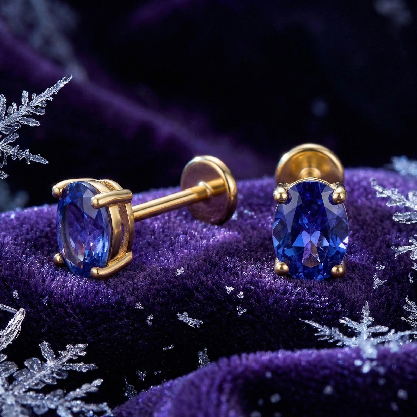 Oval cut simulated tanzanite stud earrings in 18K gold vermeil on purple velvet with snowflakes.