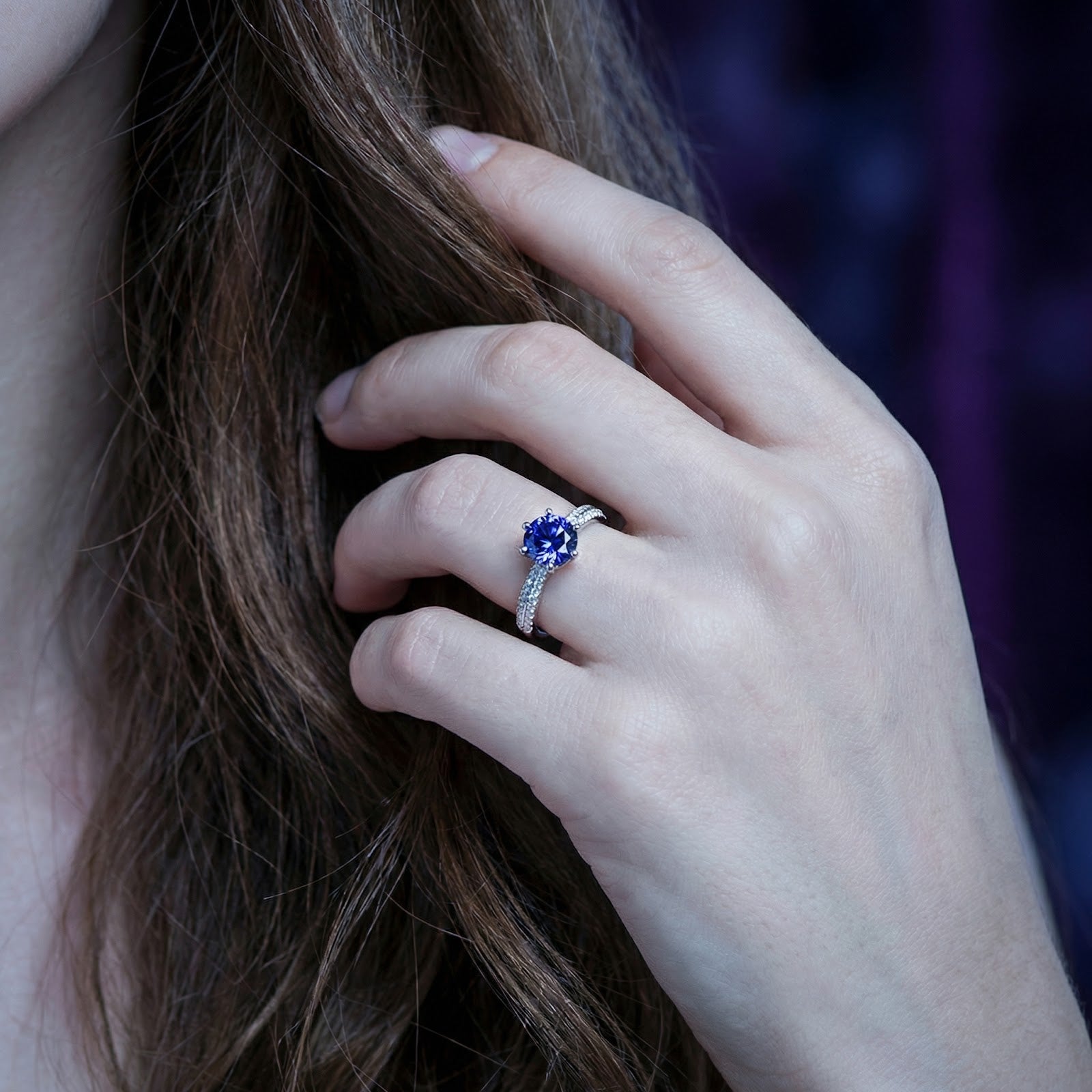 Sterling silver simulated tanzanite solitaire ring shown on a model's finger with a purple background.