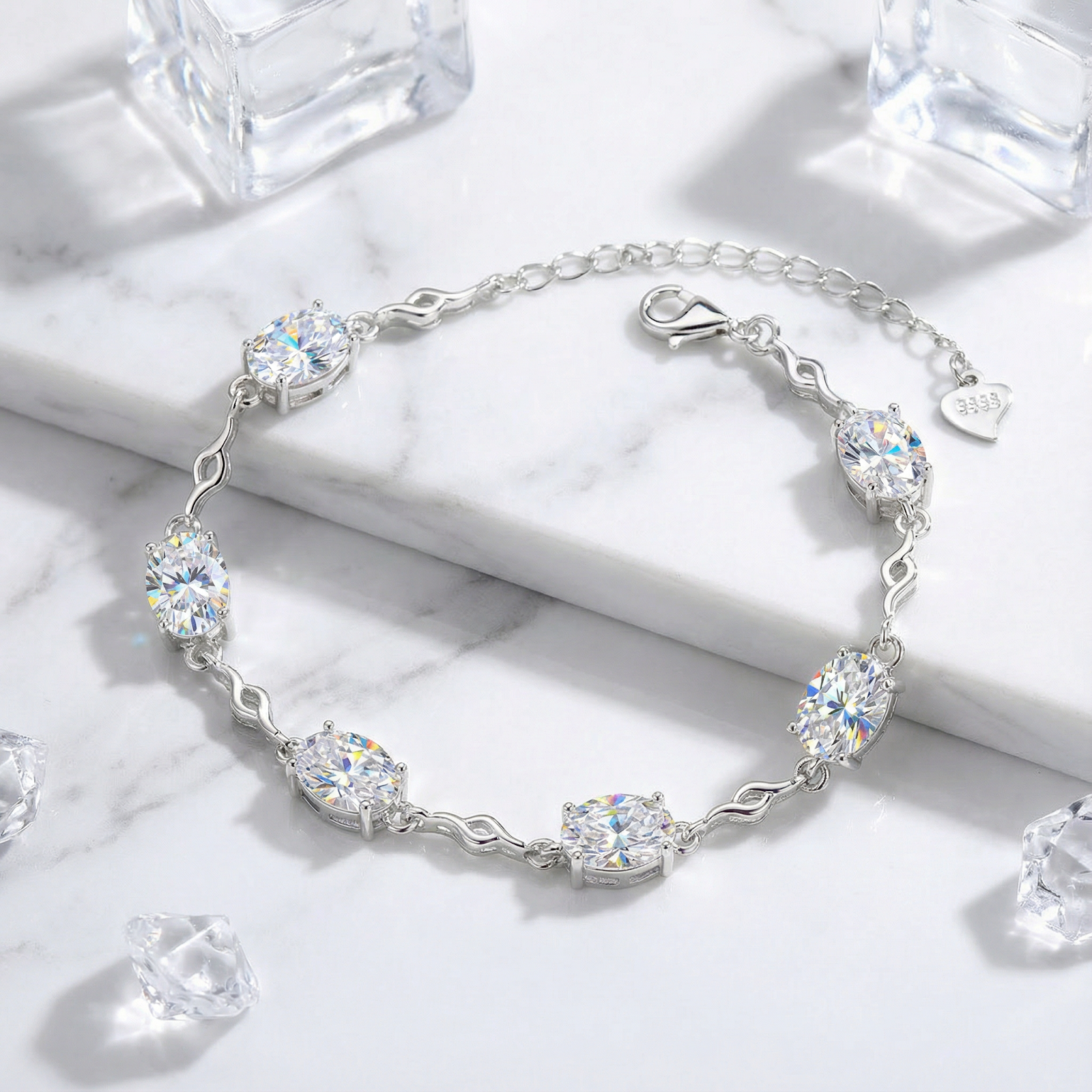 Sterling silver station bracelet with oval zirconia stones on a marble surface with decorative ice cubes.