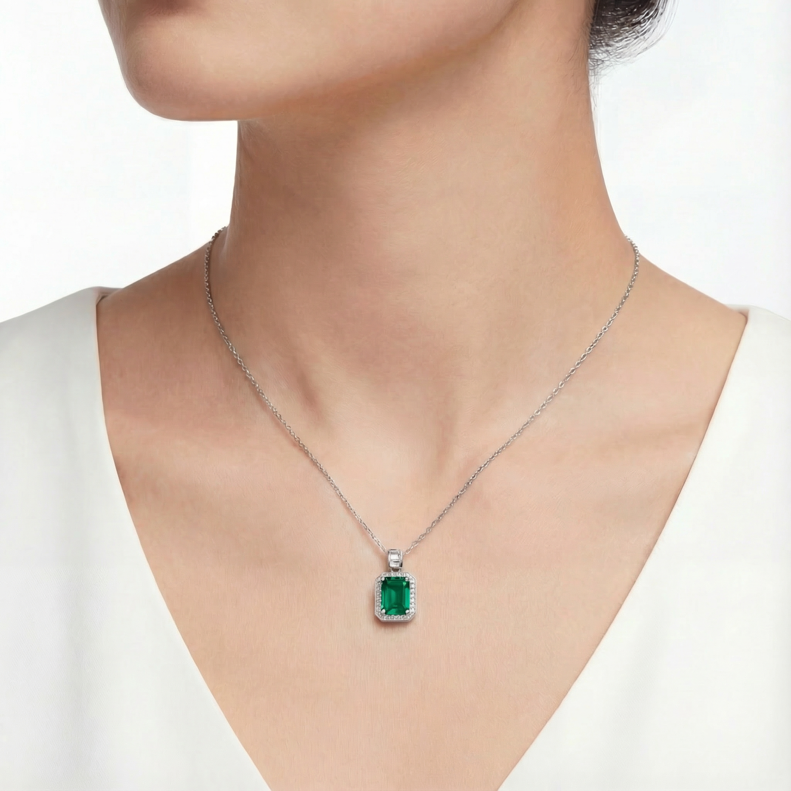Woman wearing the Elisandra emerald-cut simulated emerald necklace in sterling silver against a white top.