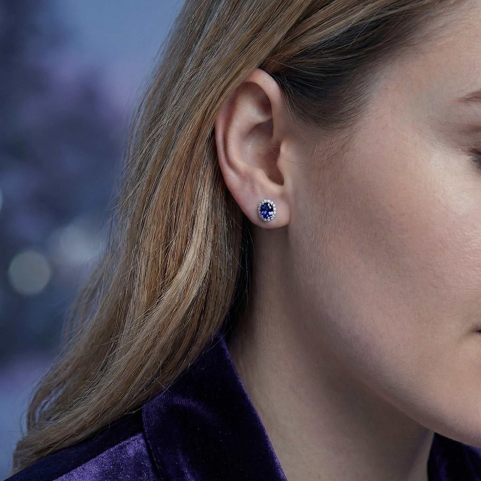 Side view of a model wearing the Lucerise oval simulated tanzanite halo earring in sterling silver.