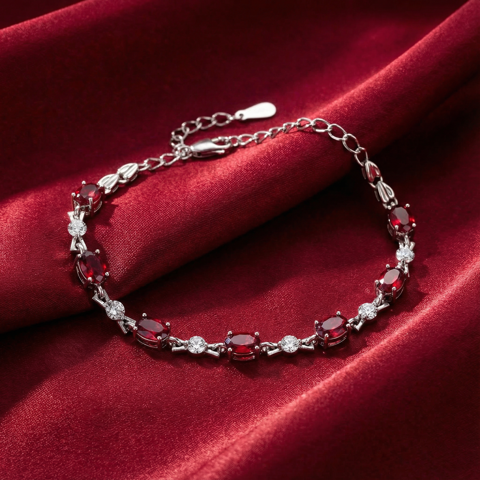 Vivara oval-cut simulated ruby tennis bracelet in S925 sterling silver on a red silk background.