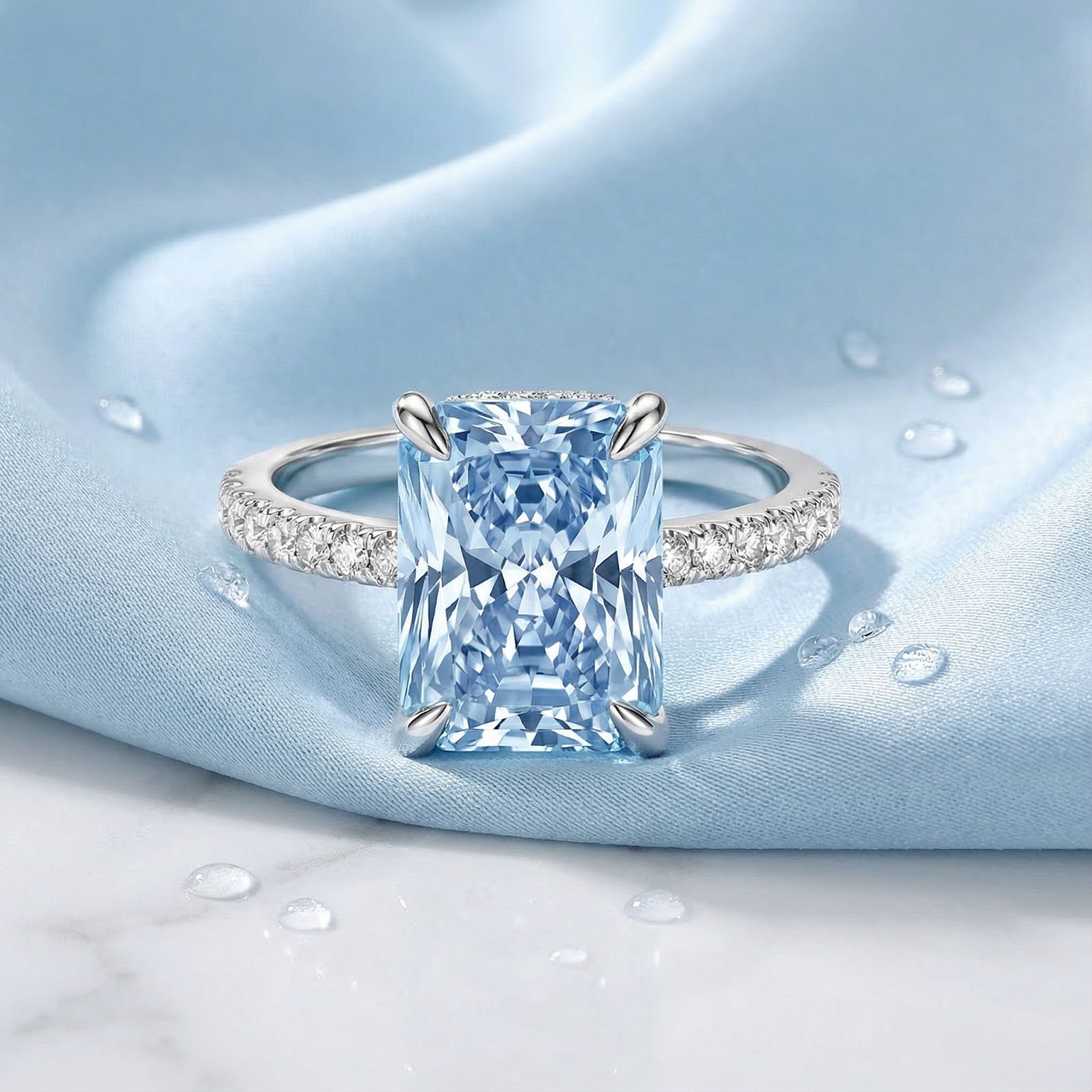 Radiant-cut simulated aquamarine ring in S925 sterling silver on light blue silk with water droplets.