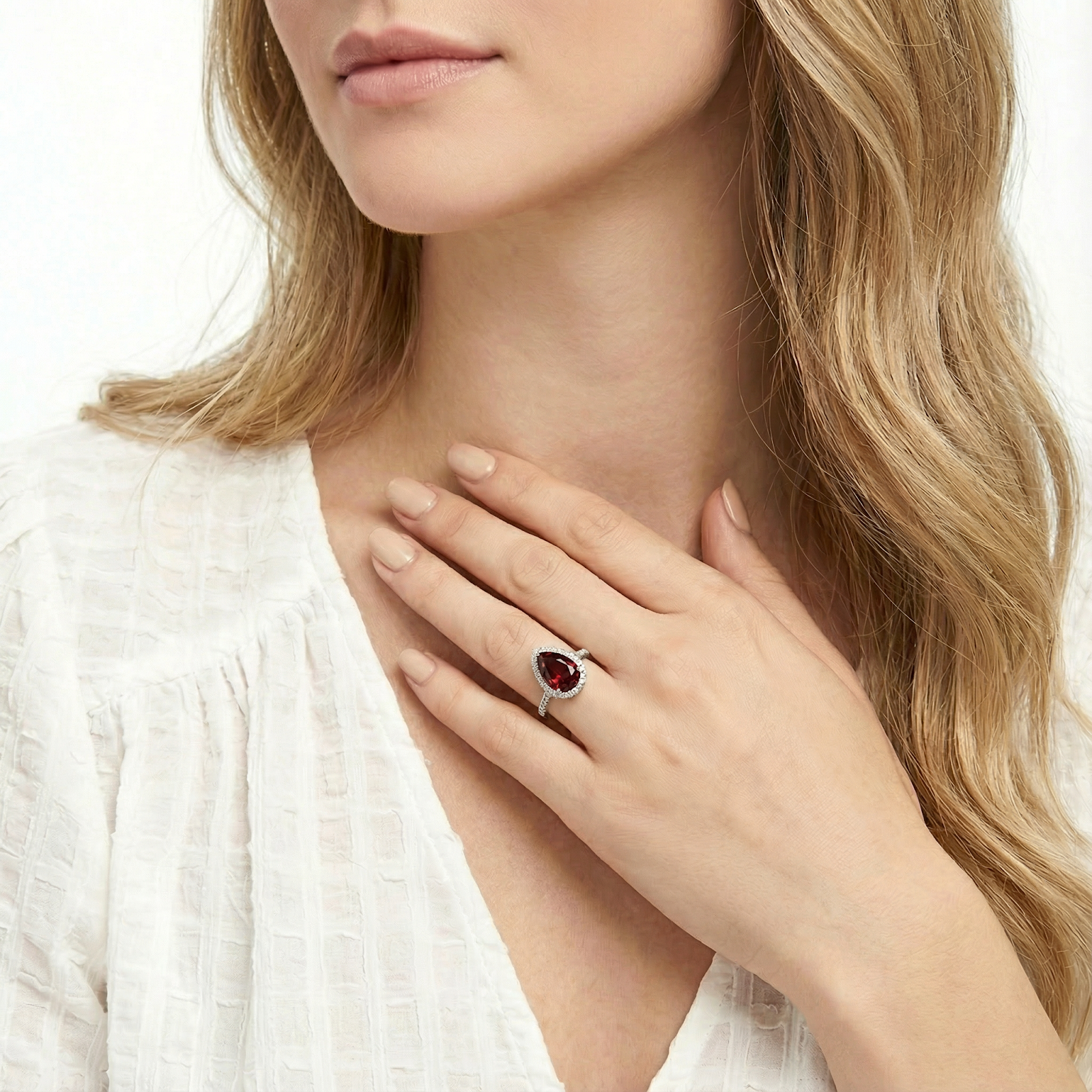 Model wearing the pear-shaped simulated garnet halo ring in sterling silver, hand resting near her neck.
