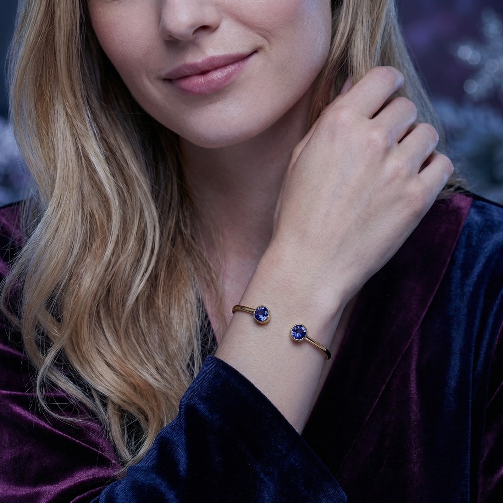 Model wearing the gold stainless steel Veralis cuff with round blue simulated tanzanite stones on her wrist.