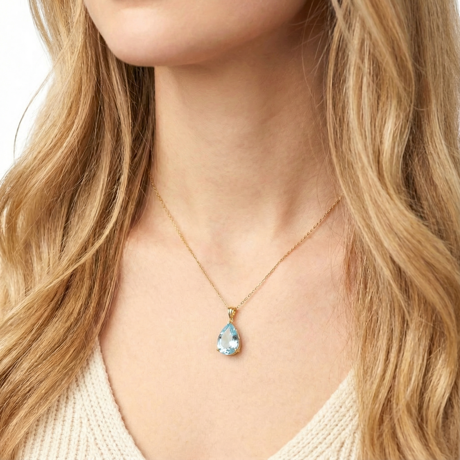 Close-up of a pear cut simulated aquamarine teardrop pendant in 18K gold vermeil worn on a neck.