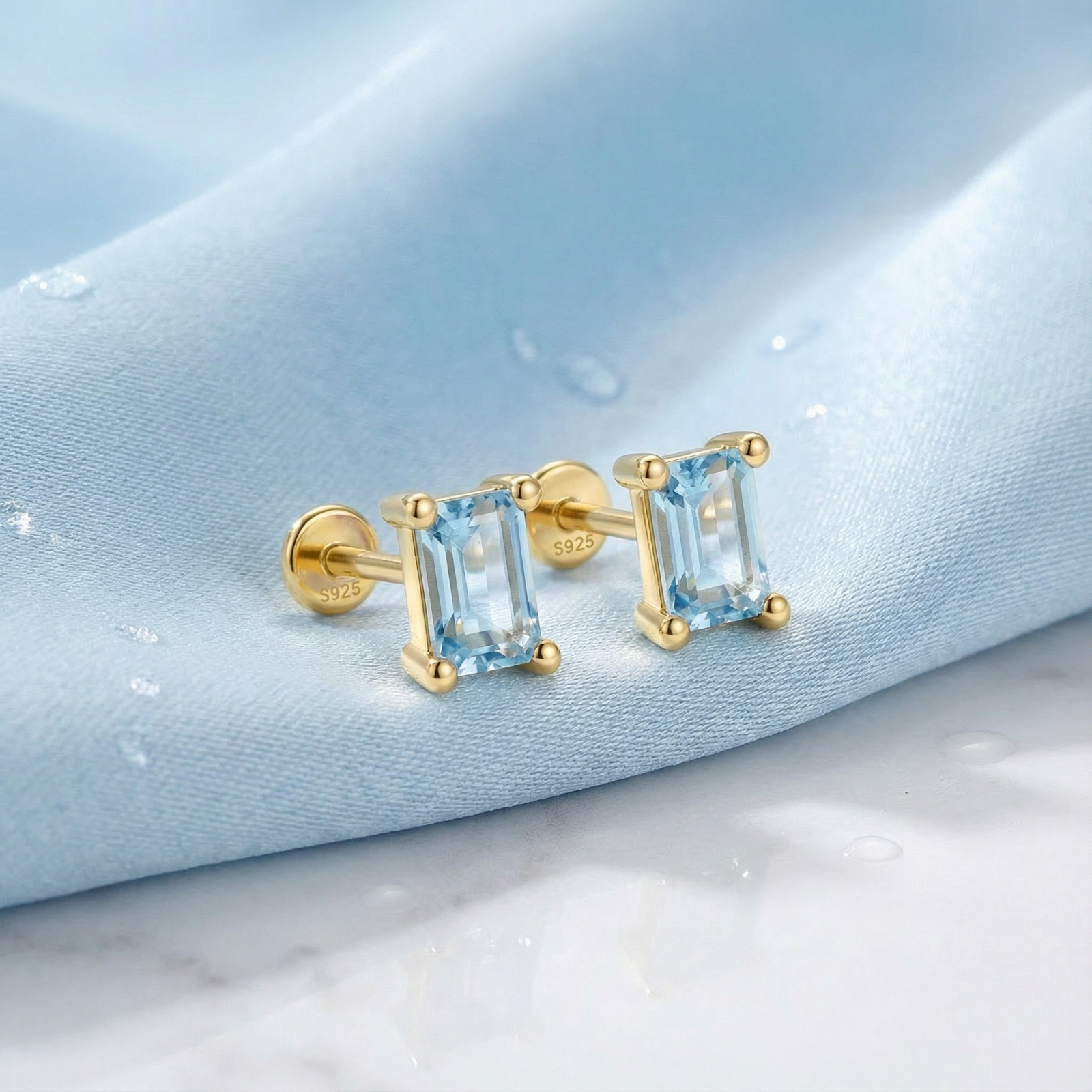 Baguette-cut simulated aquamarine earrings in 18K gold vermeil resting on light blue silk fabric.