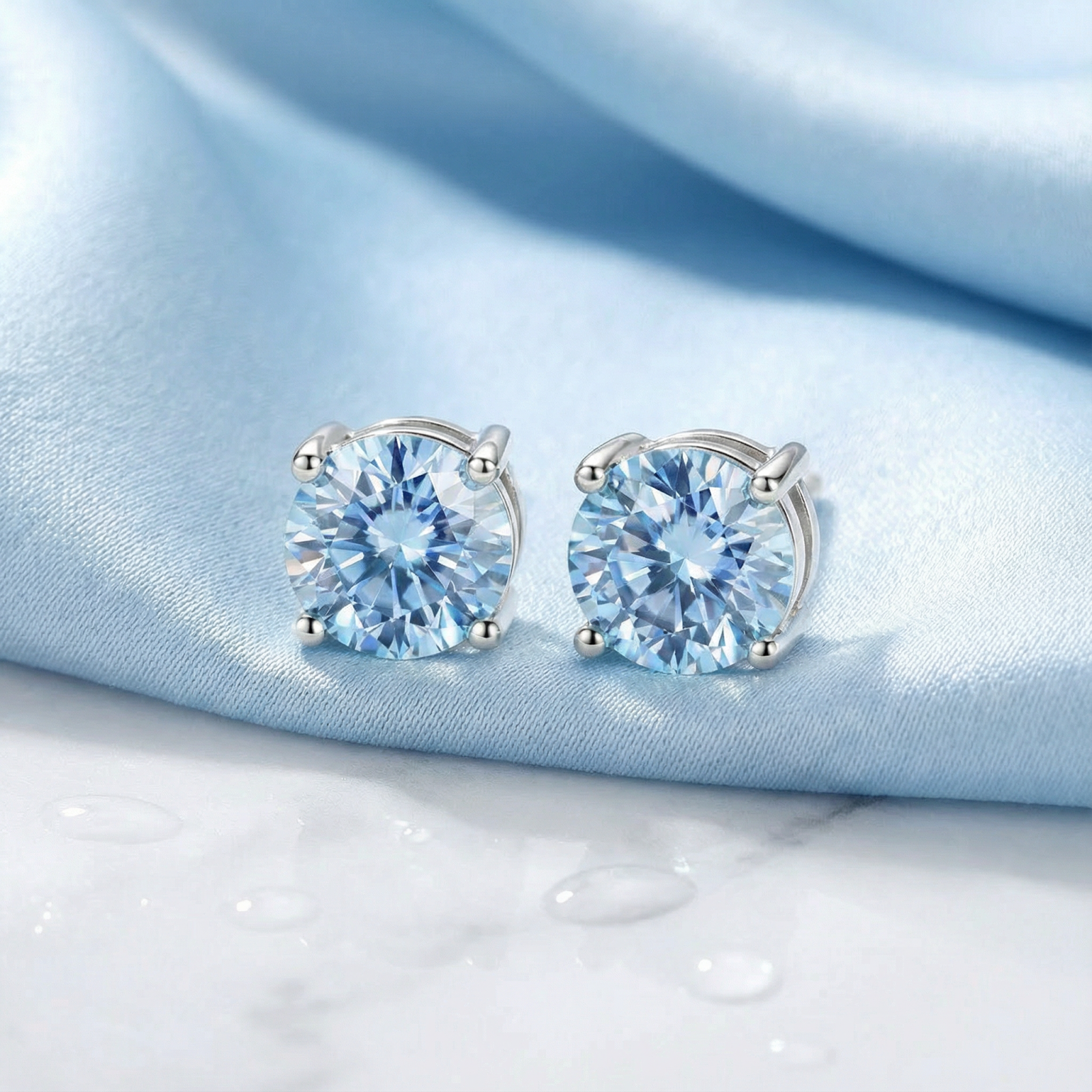 Round cut simulated aquamarine stud earrings in sterling silver on light blue silk with water droplets.