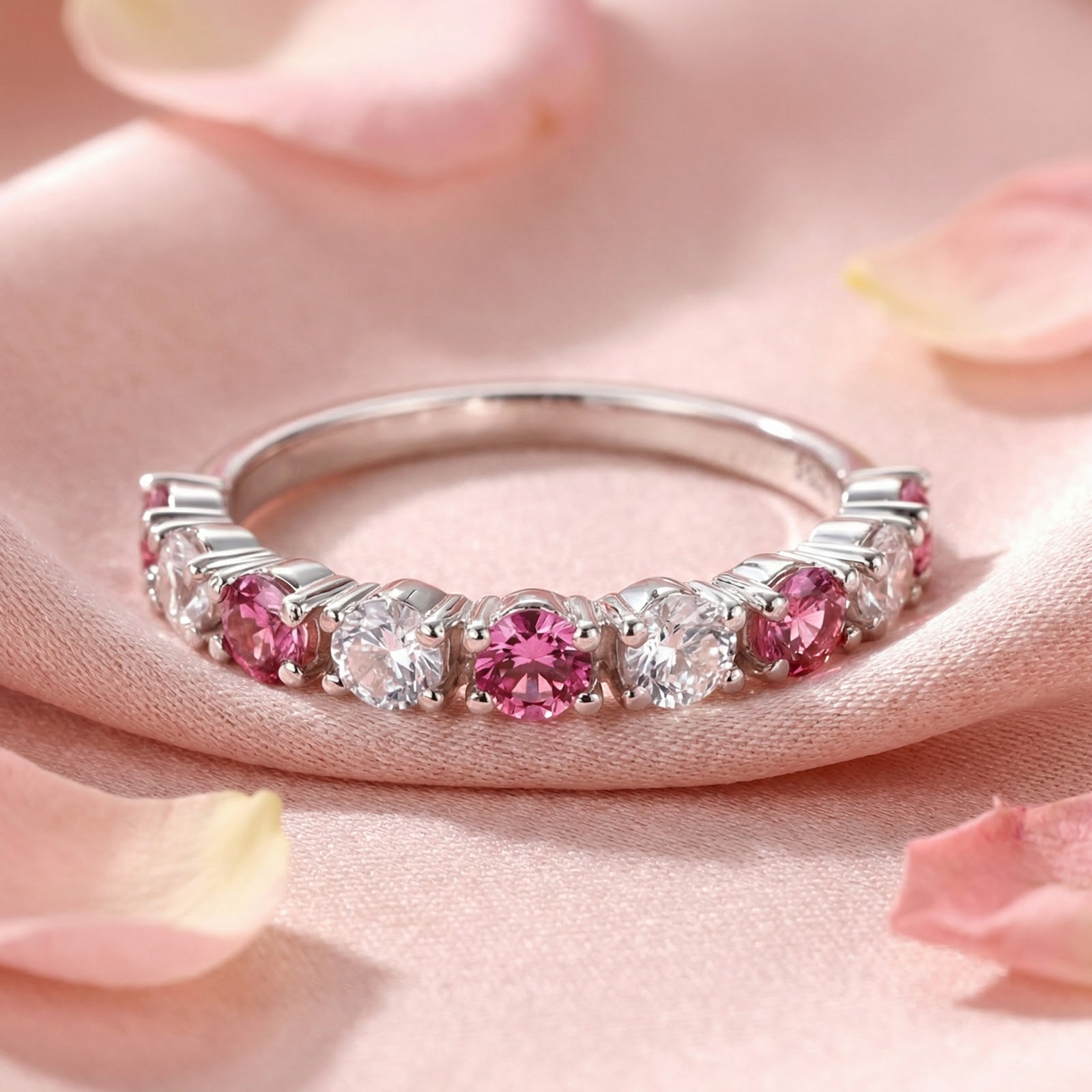 Sterling silver ring with round-cut pink tourmaline and clear stones in a macro detail shot on pink fabric.