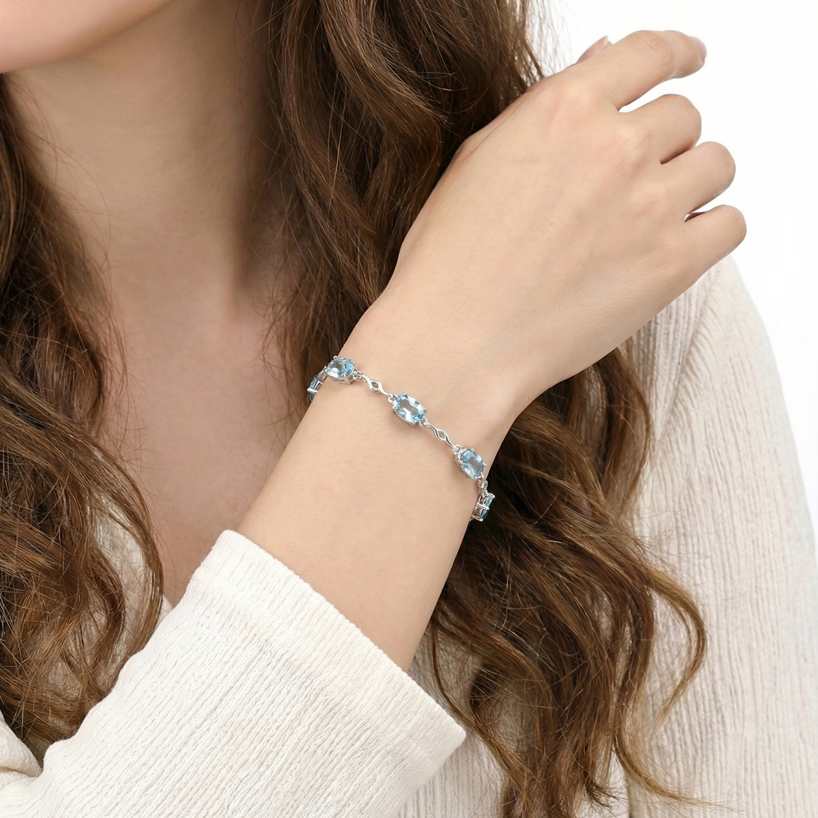 Sterling silver station bracelet with oval simulated aquamarine stones worn on a woman's wrist.