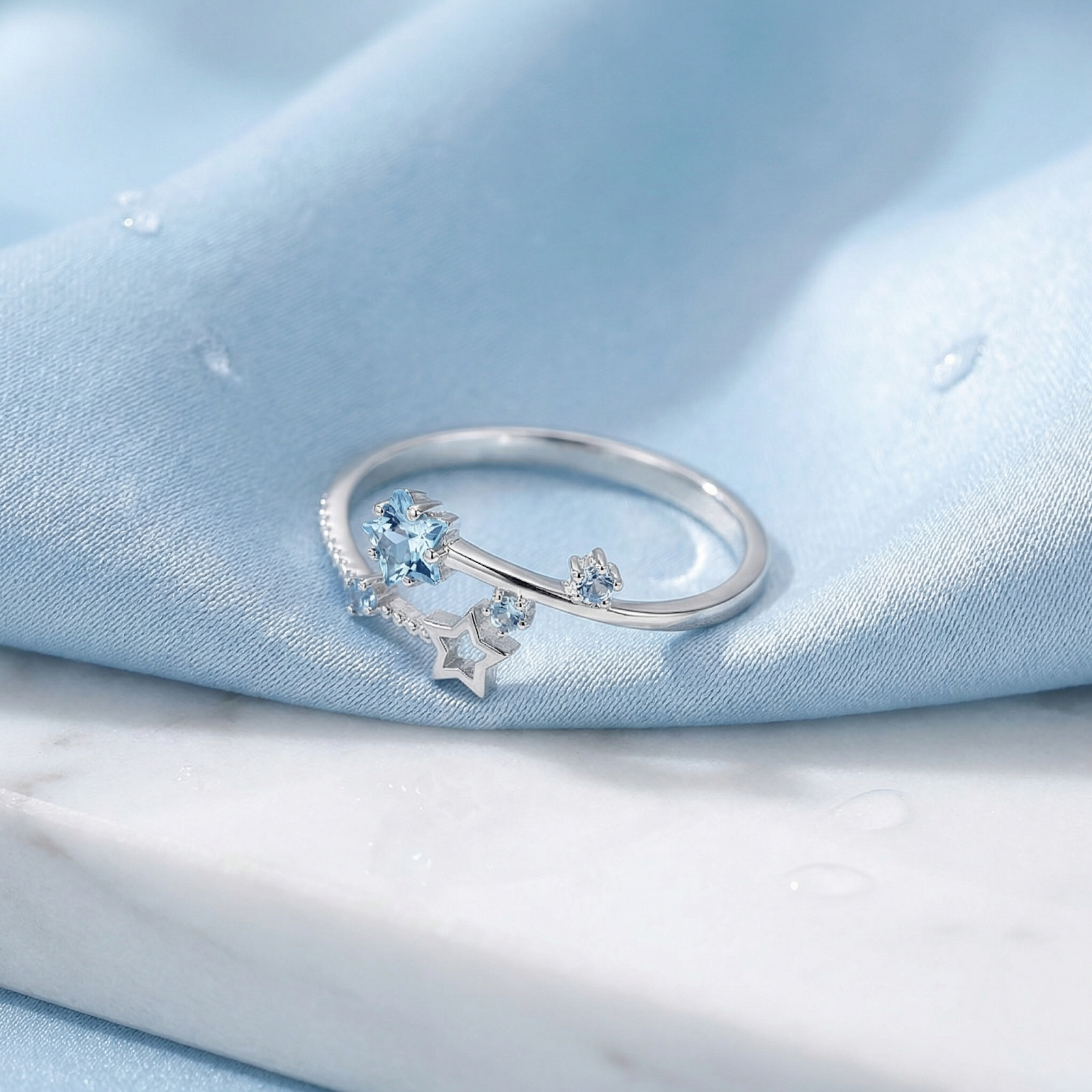 Sterling silver Stella bypass ring with star-shaped simulated aquamarine stones on a blue silk background.