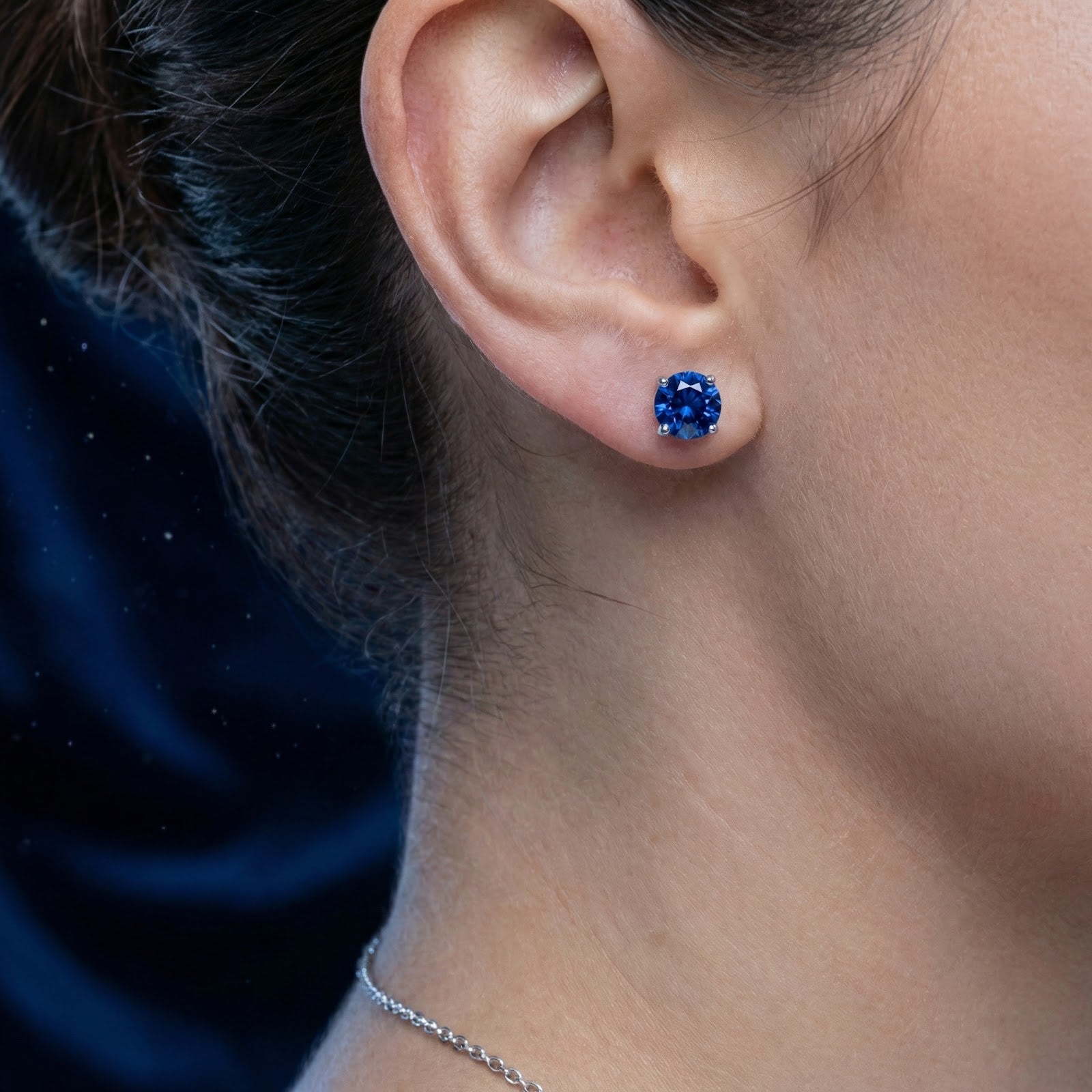 Close-up of a woman wearing a round cut royal blue simulated sapphire stud earring in 925 sterling silver.