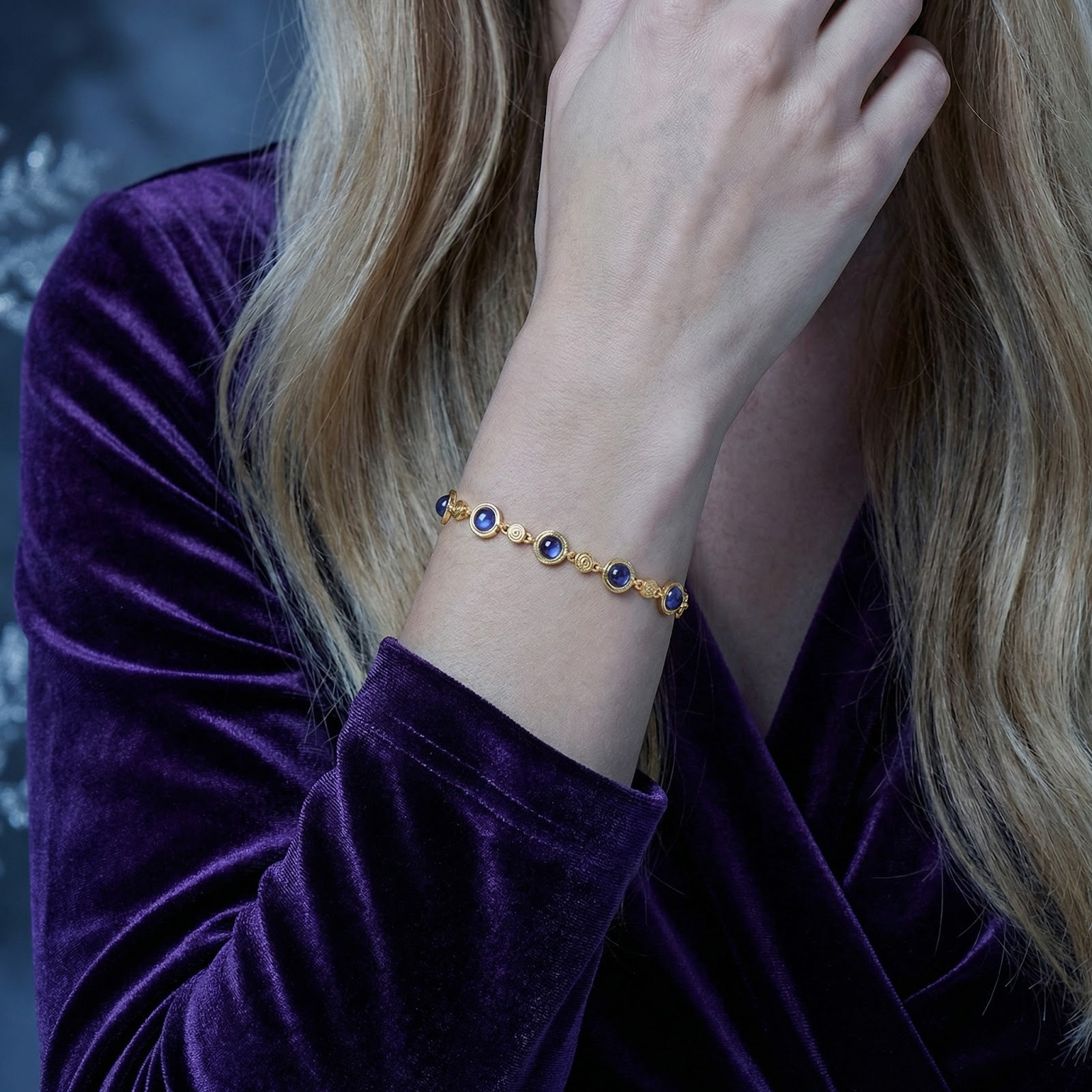 A woman's wrist adorned with the 18K gold vermeil station bracelet and round simulated tanzanite stones.