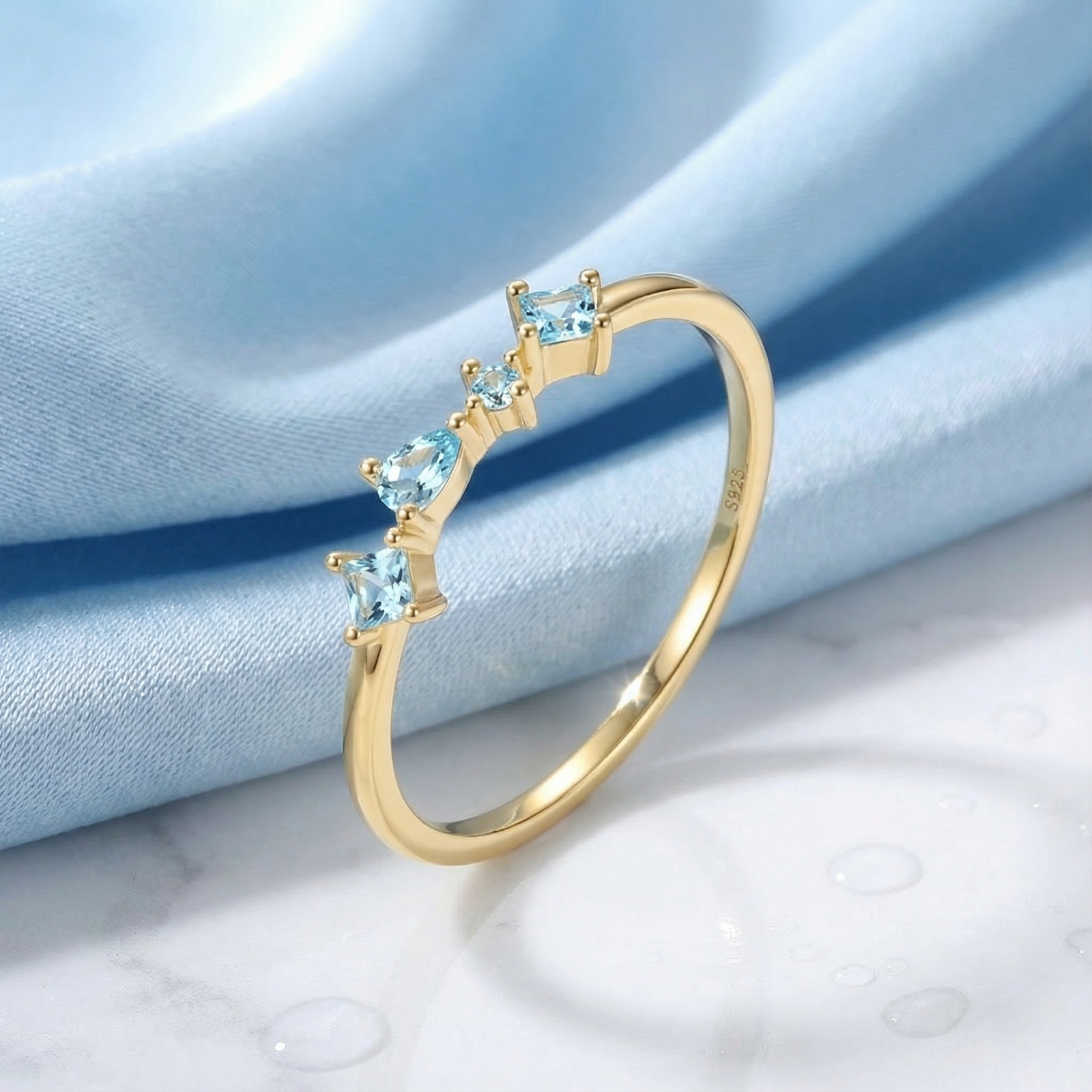 18K gold vermeil cluster ring with pear and square cut light blue simulated aquamarine stones on blue fabric.