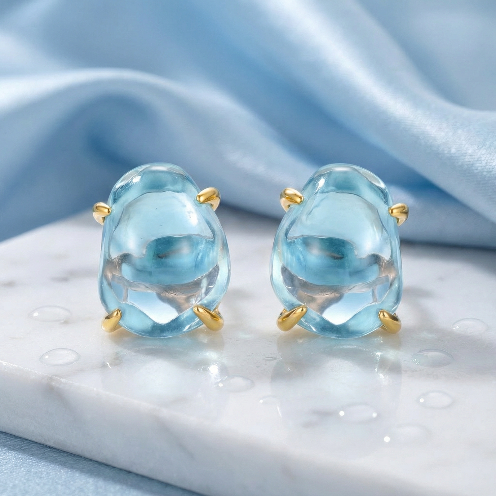 Organic cut March birthstone simulated aquamarine stud earrings in 18K gold vermeil settings on white marble.