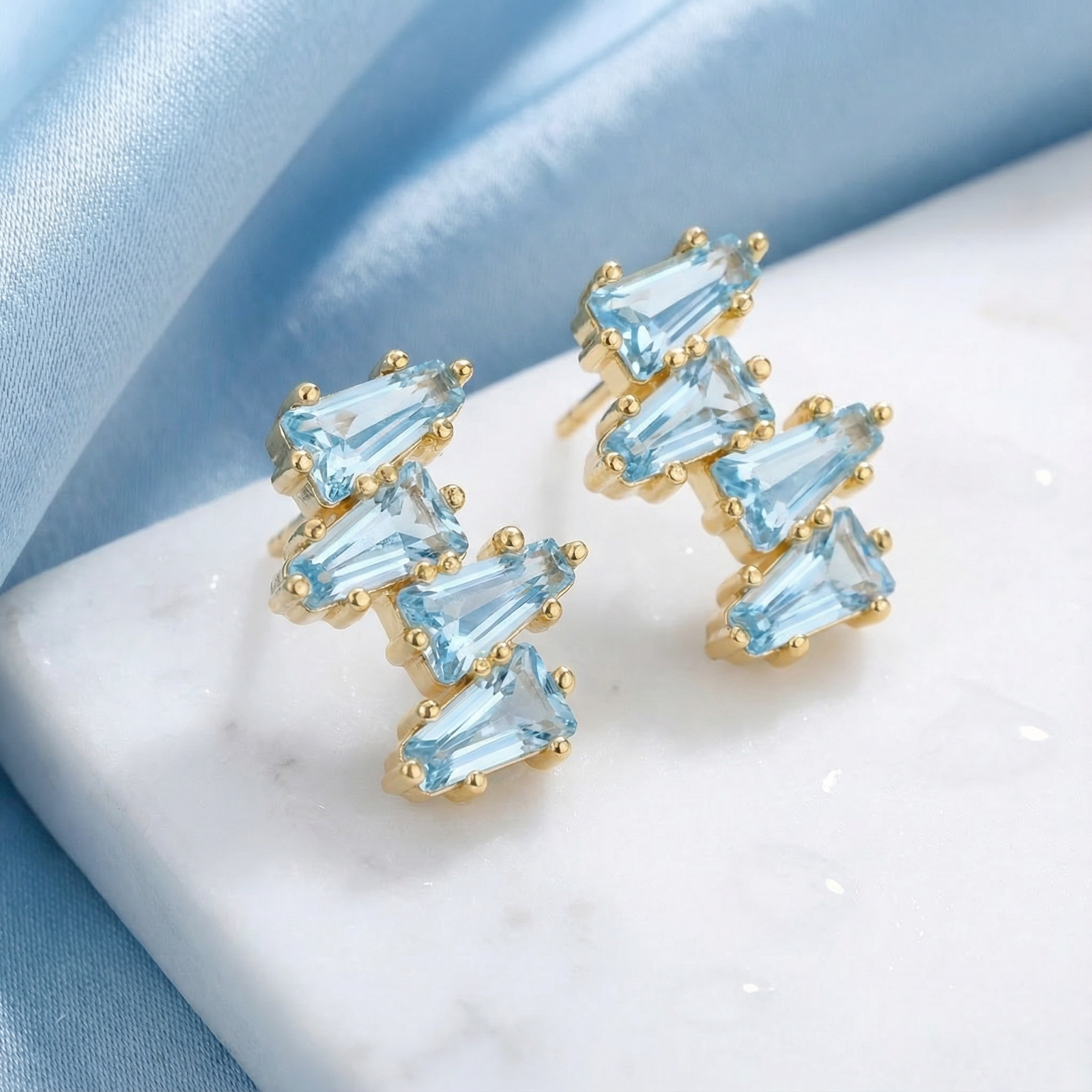 Lyraea Cluster earrings in 18K gold vermeil with baguette-cut simulated aquamarine on marble and blue silk.