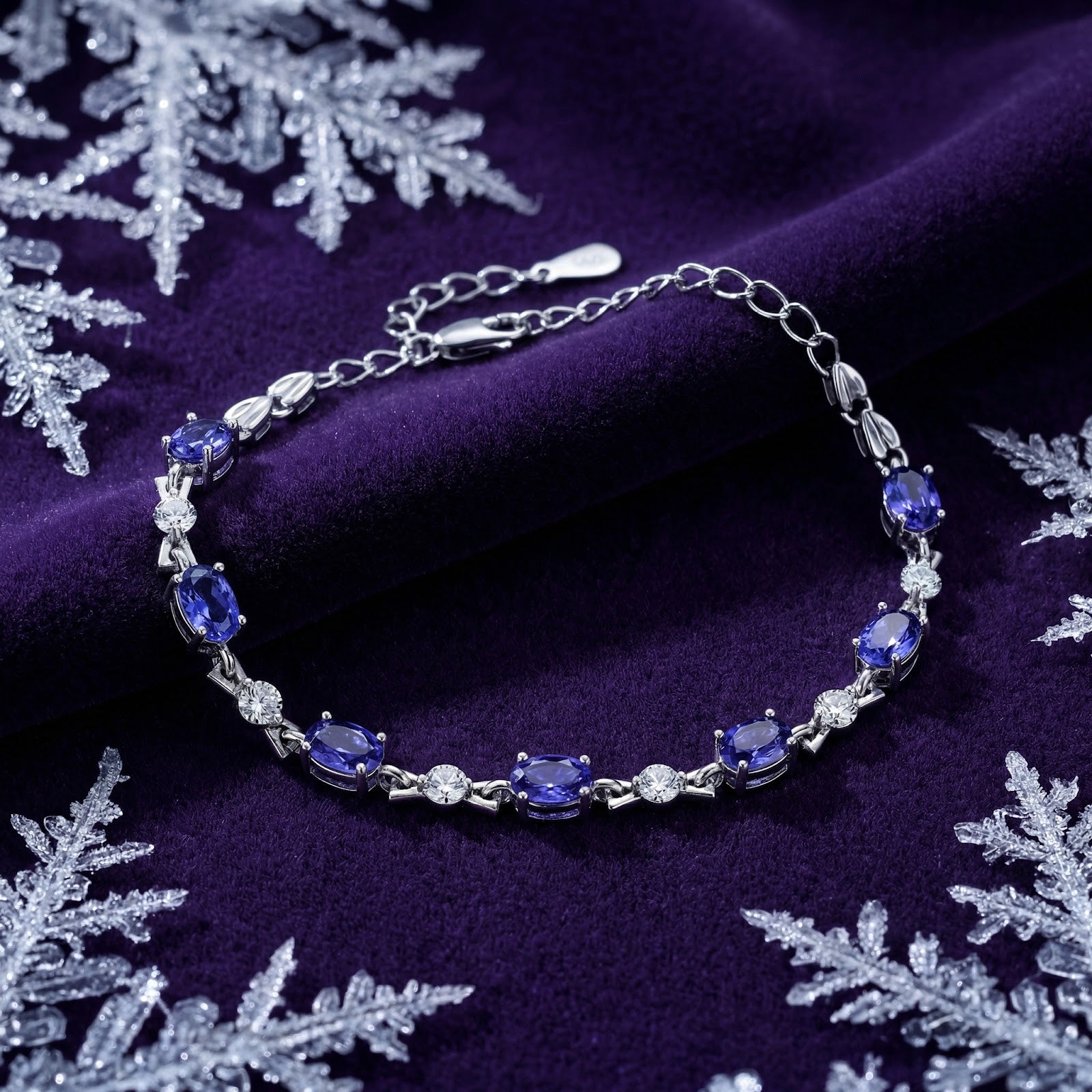 Oval simulated tanzanite sterling silver bracelet on purple velvet with decorative winter snowflakes.