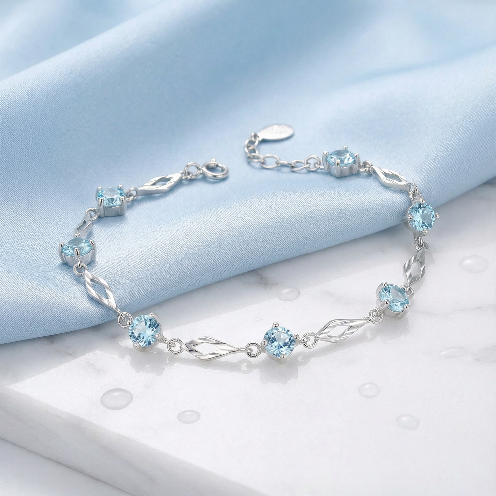 Etherea station bracelet in S925 sterling silver with round-cut simulated aquamarine on blue silk and marble.