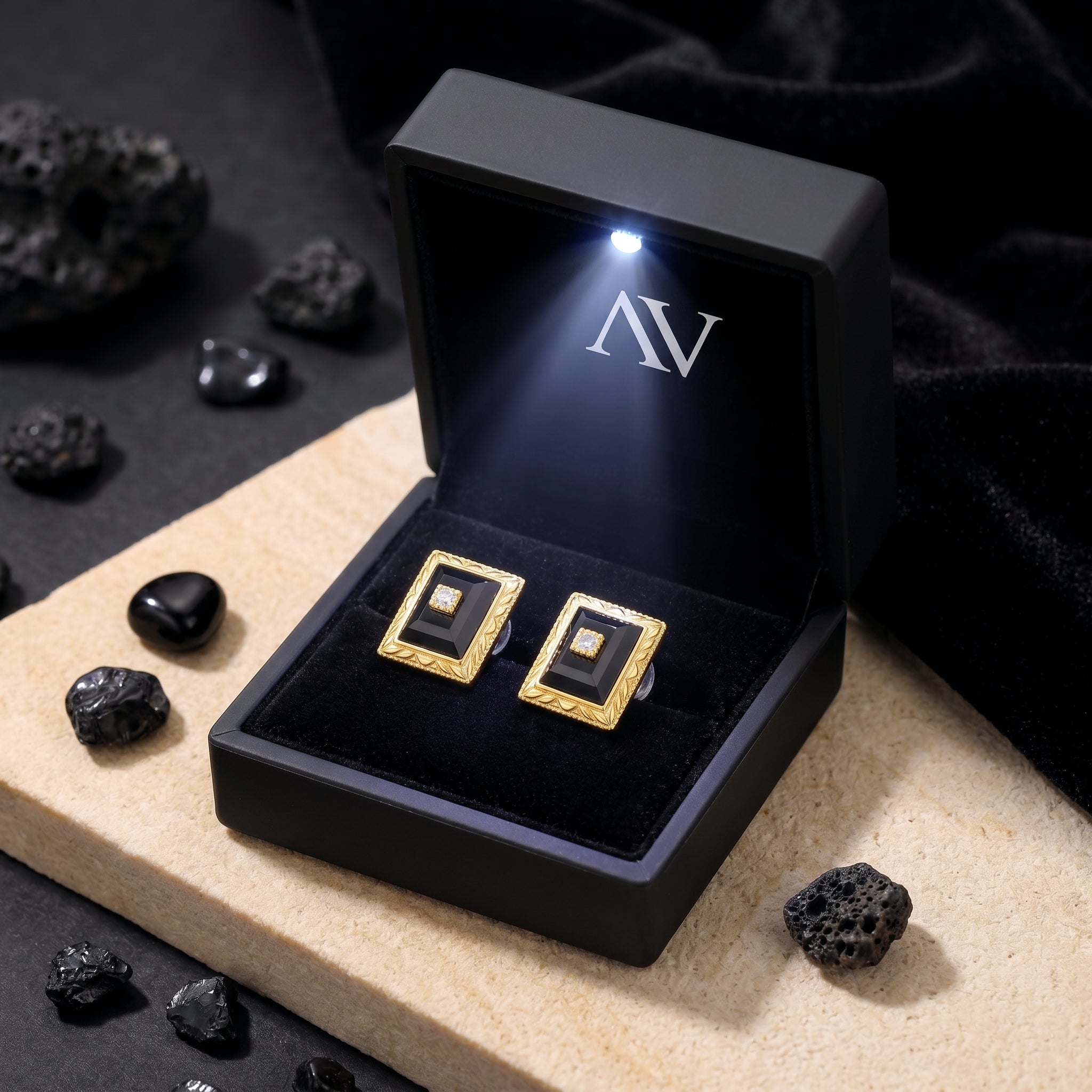Yellow gold square-cut onyx earrings presented in a black illuminated jewelry gift box on a stone surface.