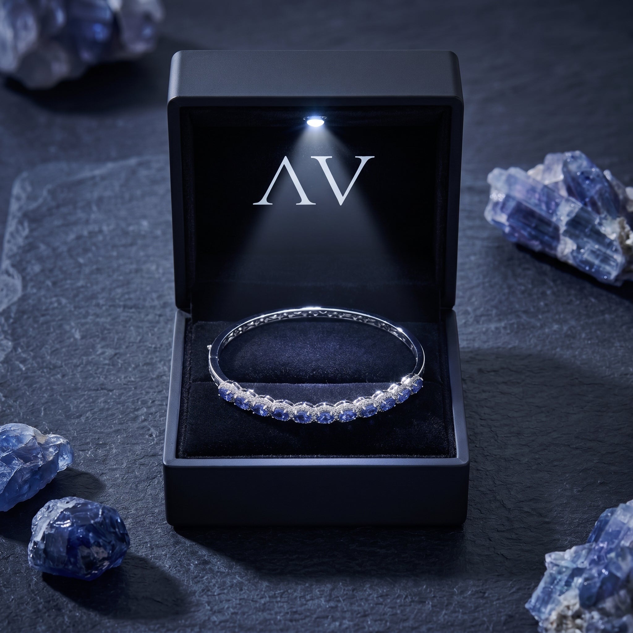 The Alvira tanzanite bangle inside a black LED-lit presentation box with raw gemstone accents.