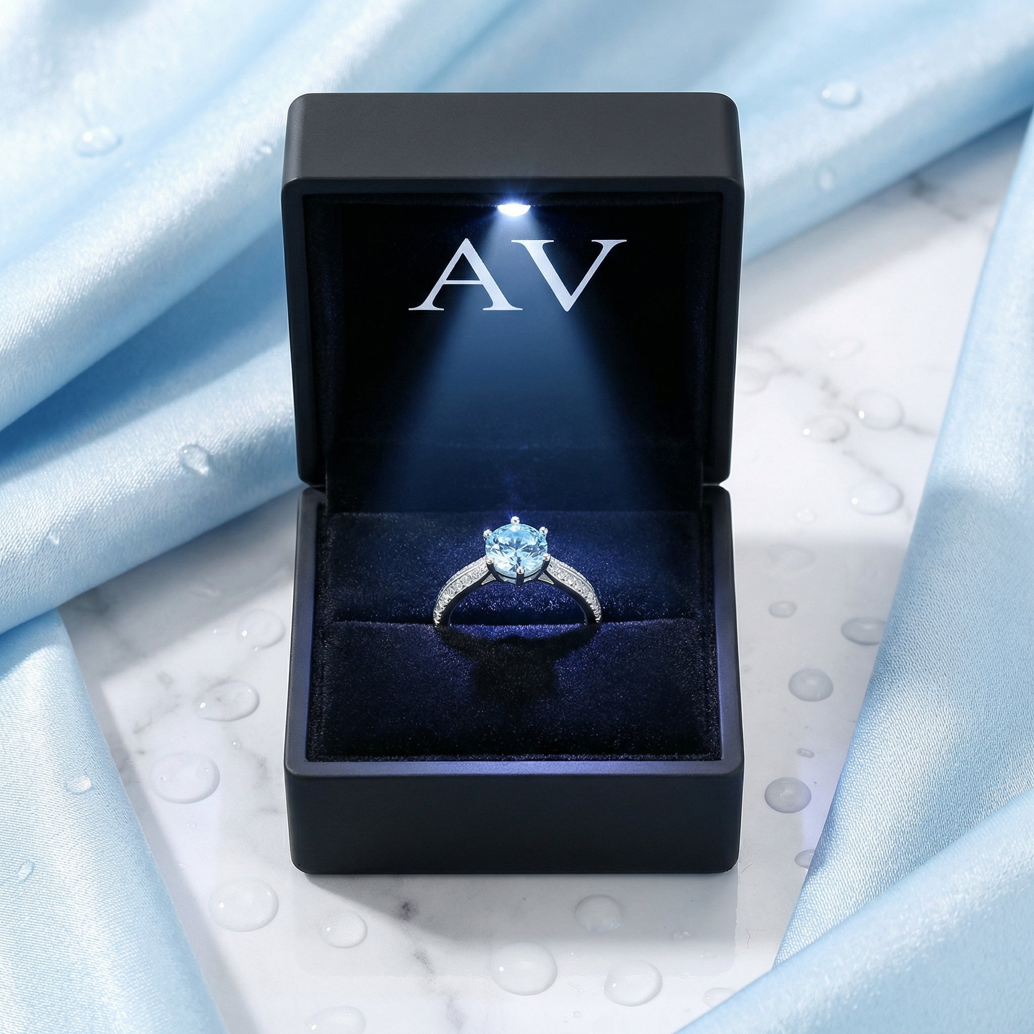 Round simulated aquamarine sterling silver ring inside a black LED-lit jewelry gift box with AV logo.