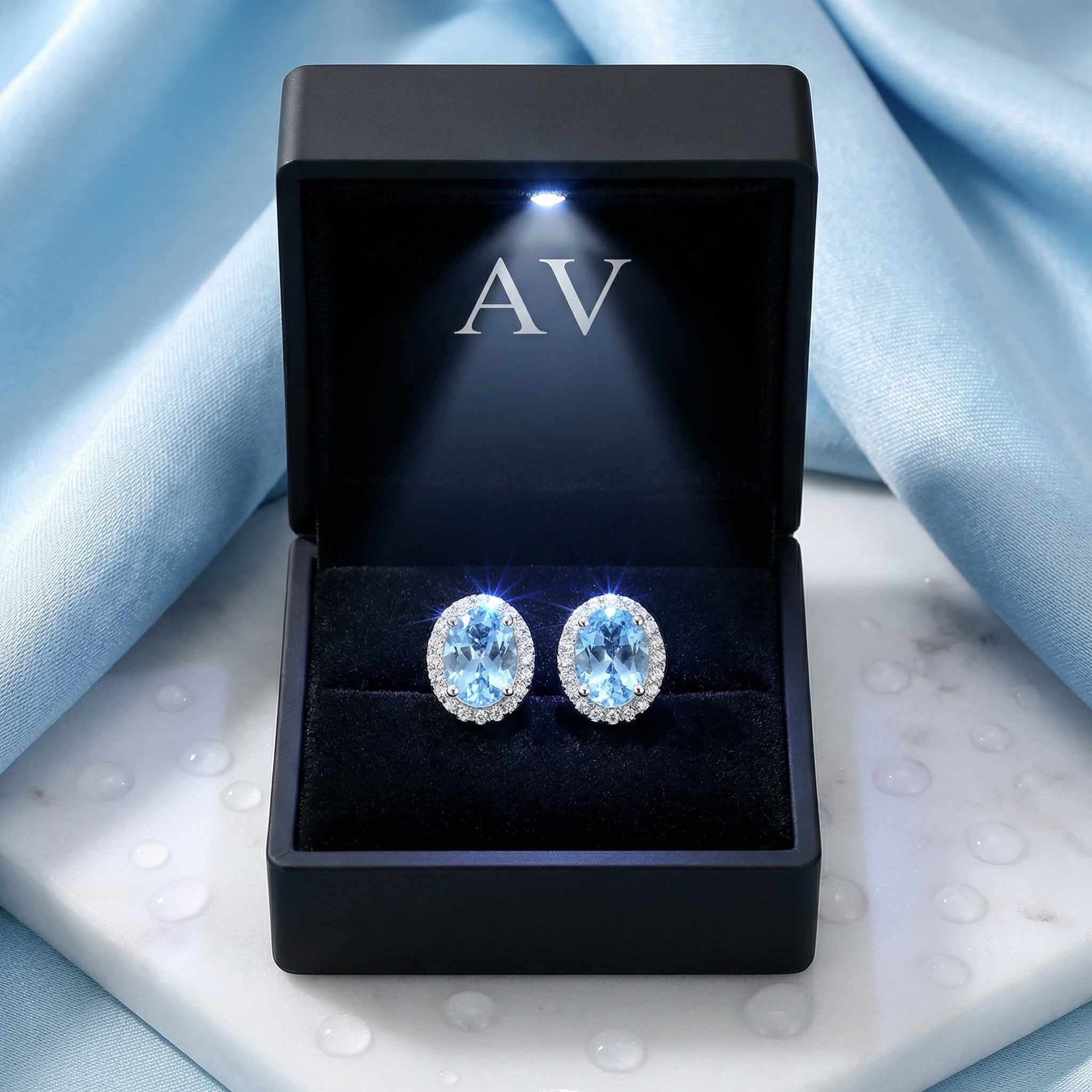 Oval simulated aquamarine halo studs in sterling silver presented in a premium lighted black jewelry box.