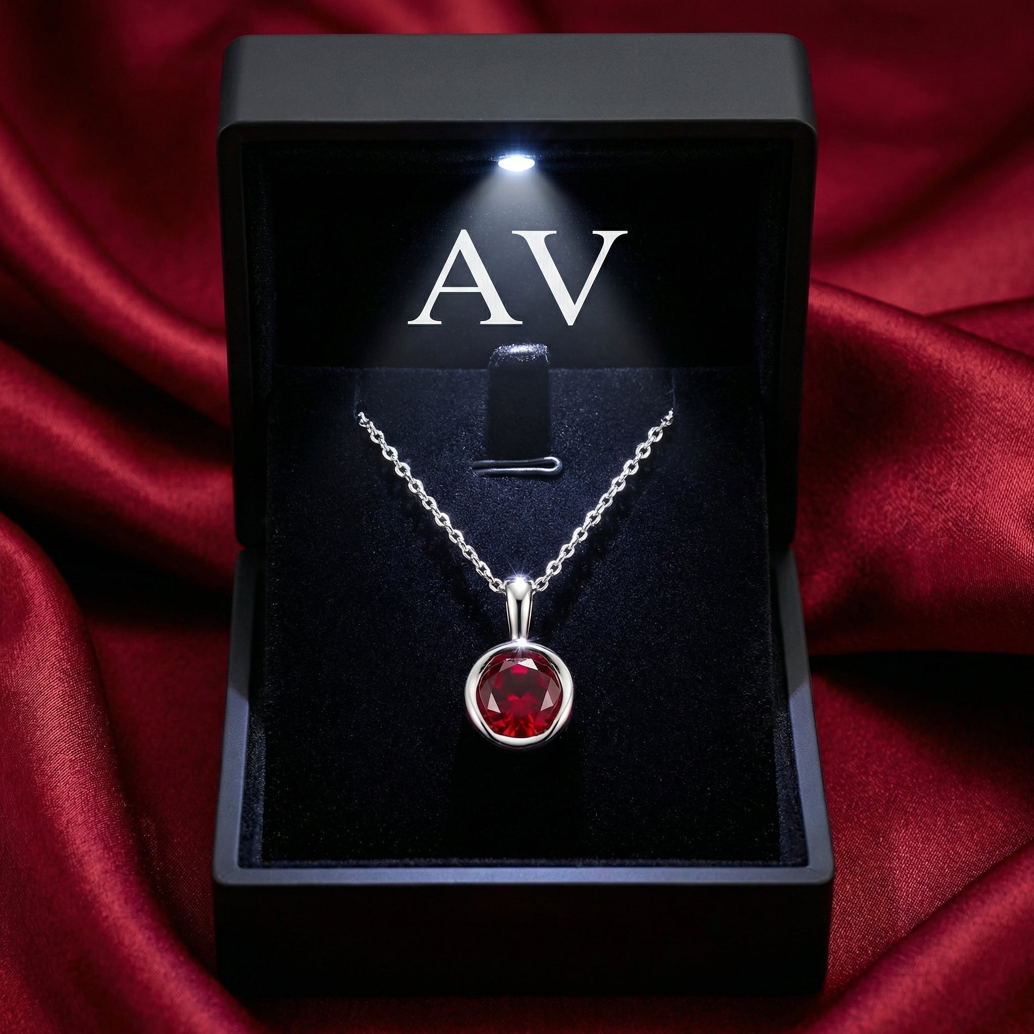 Simulated ruby pendant in a sterling silver setting inside a lighted black jewelry gift box.