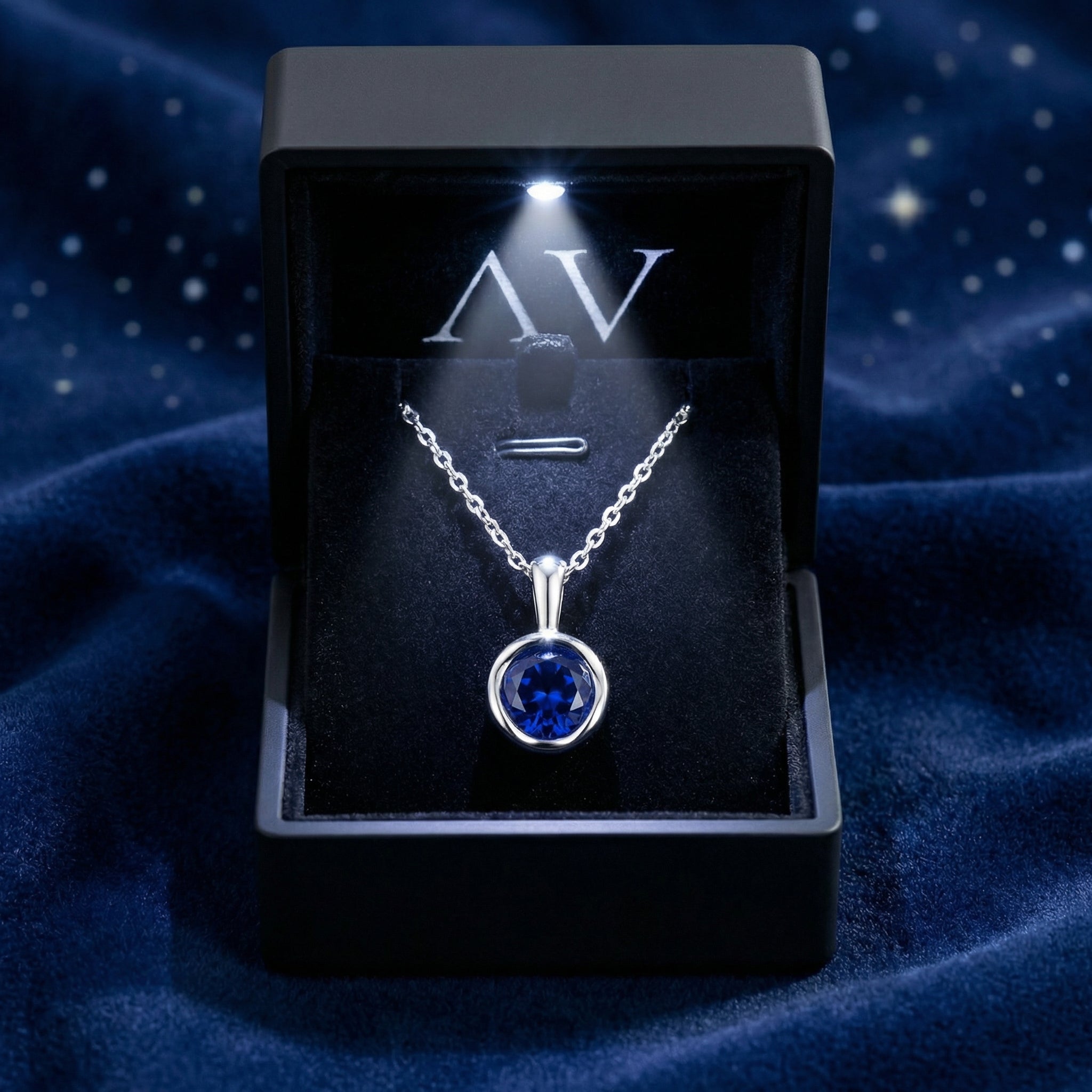 Round blue simulated sapphire necklace in a sterling silver bezel setting inside a lighted black gift box.