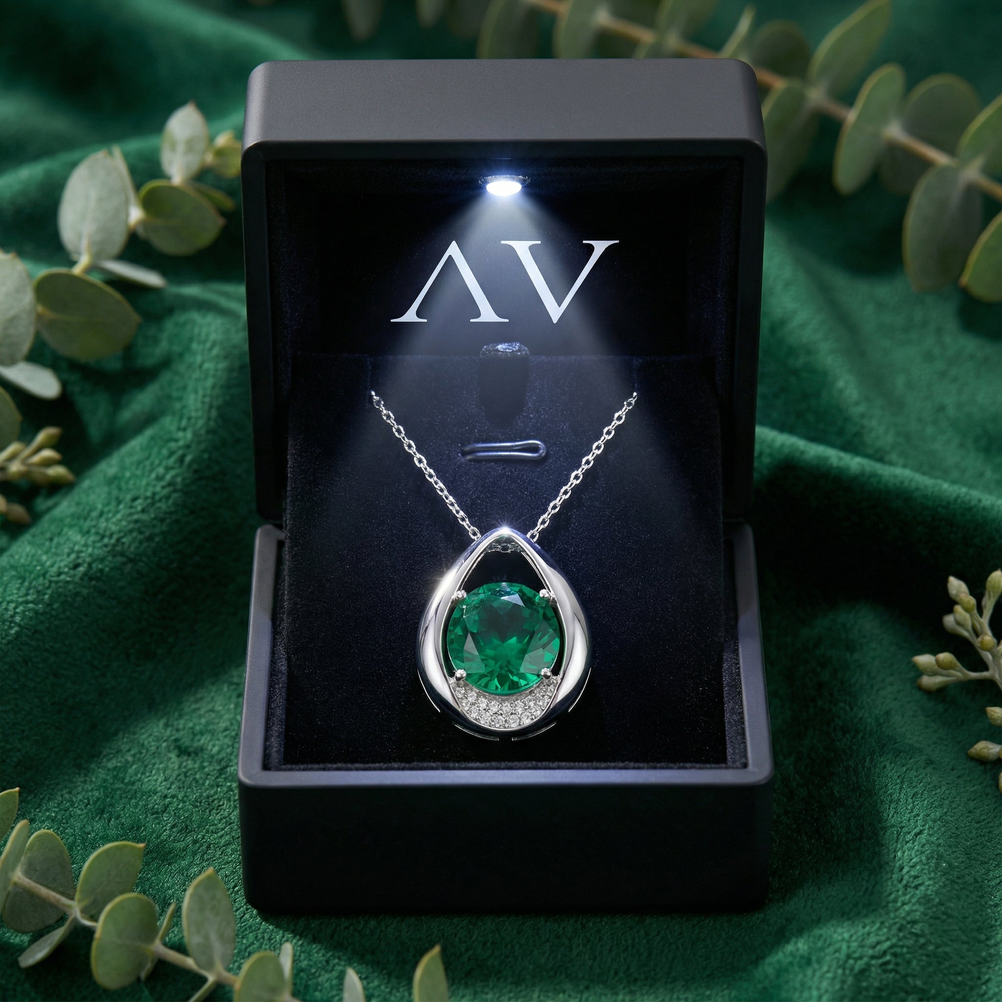 Sterling silver teardrop necklace with a round green simulated emerald in a lighted black jewelry gift box.