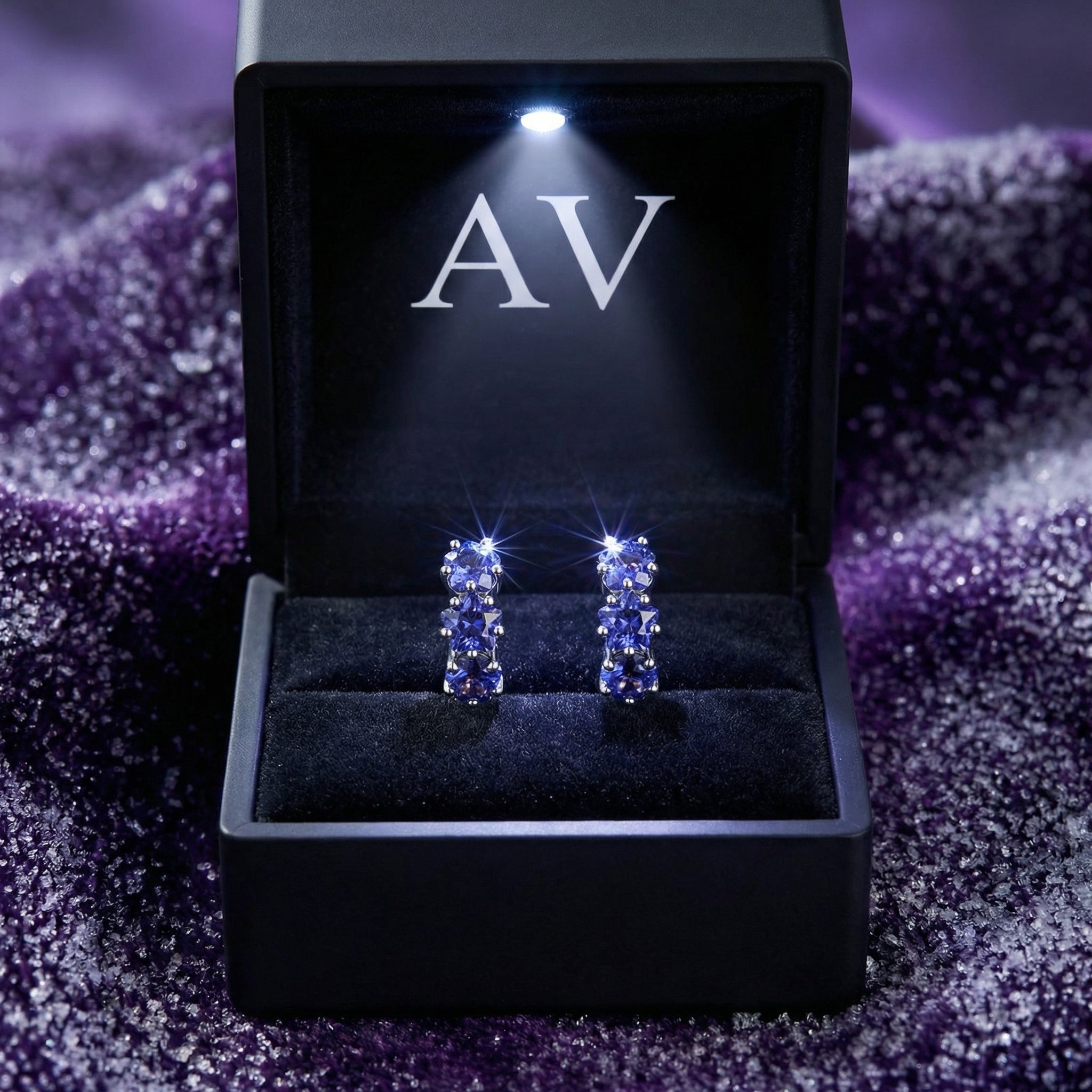 Sterling silver star huggie earrings with blue simulated tanzanite in a lighted black jewelry presentation box.