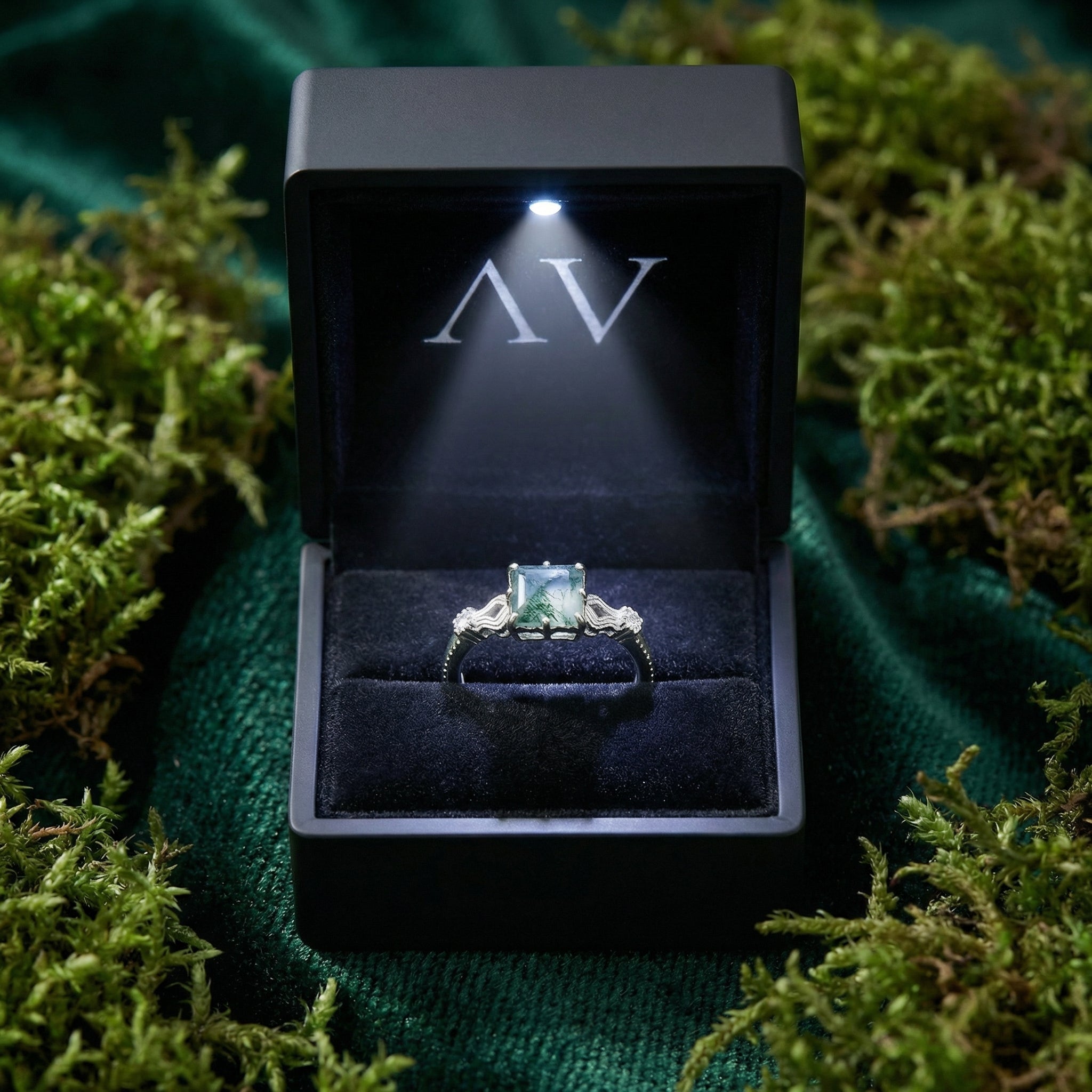 Cushion cut moss agate silver ring presented in a black lighted gift box on a bed of green moss.