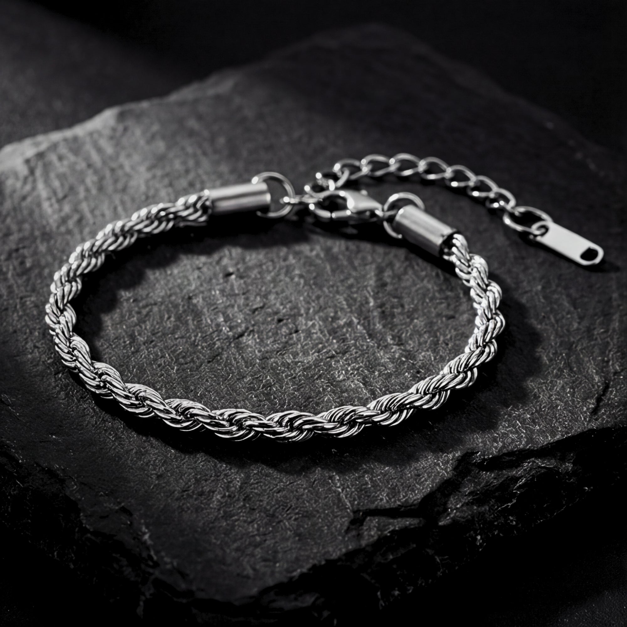 Silver stainless steel mariner rope chain bracelet with lobster clasp on a dark textured stone.