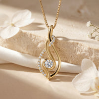 Yellow gold moissanite swirl pendant with a round solitaire on a styled stone background.