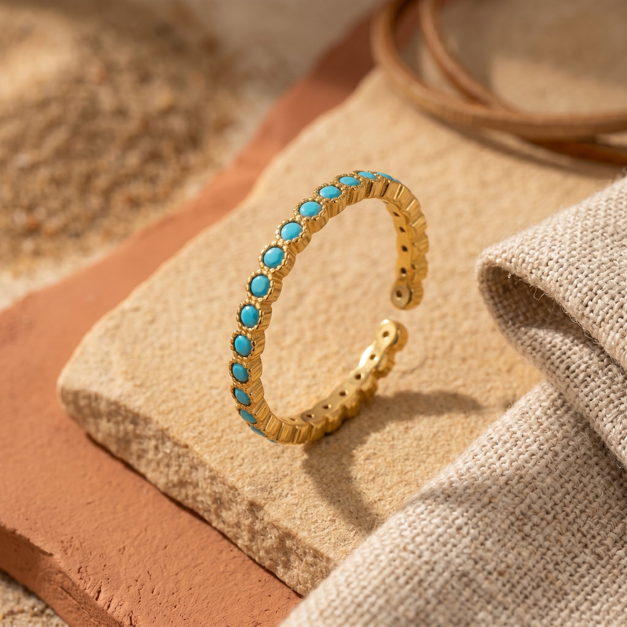 Gold Zia turquoise eternity ring with round stones on a desert-inspired stone background.
