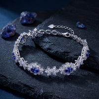 Floral tanzanite tennis bracelet in white gold on dark stone with raw tanzanite gemstones.