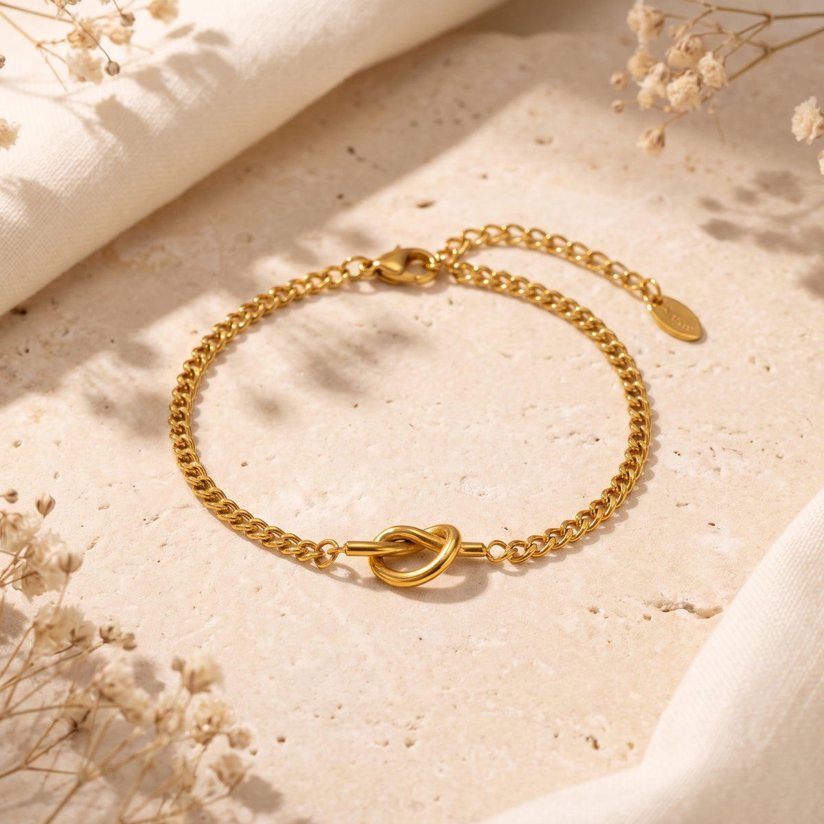 Gold-tone curb link bracelet with a central knot motif, laid flat on a textured stone surface.