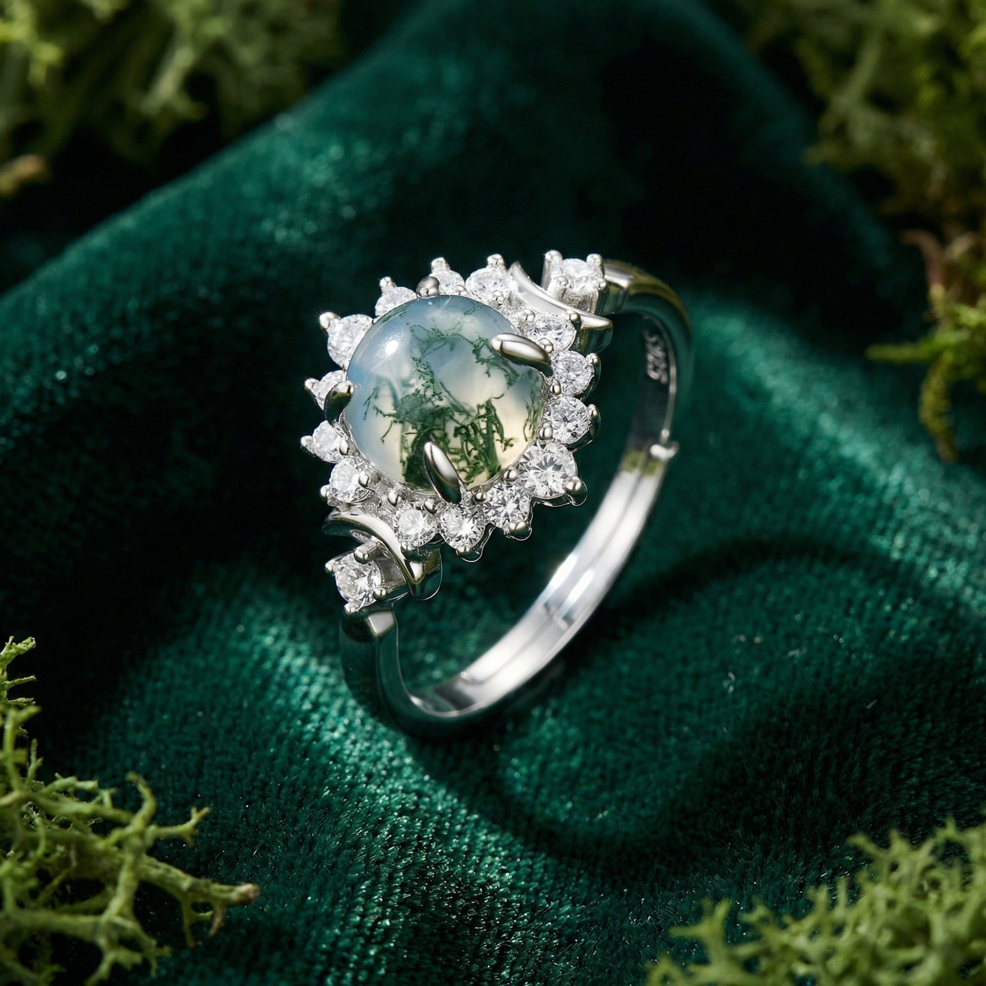 Angled view of a round moss agate cabochon ring with a floral halo in S925 sterling silver on green velvet.