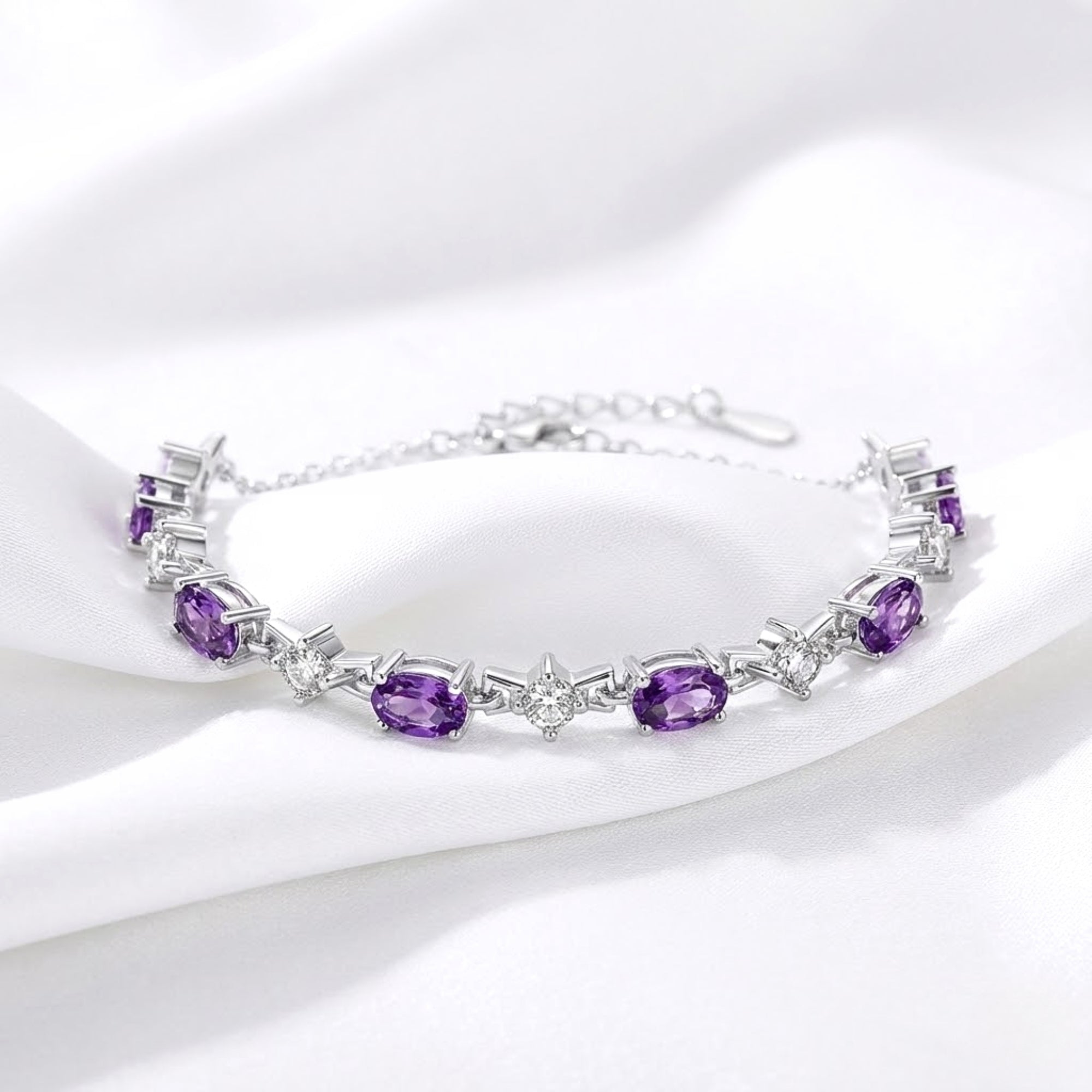 Lucina S925 sterling silver tennis bracelet with oval cut simulated amethyst and round clear stones on white fabric.