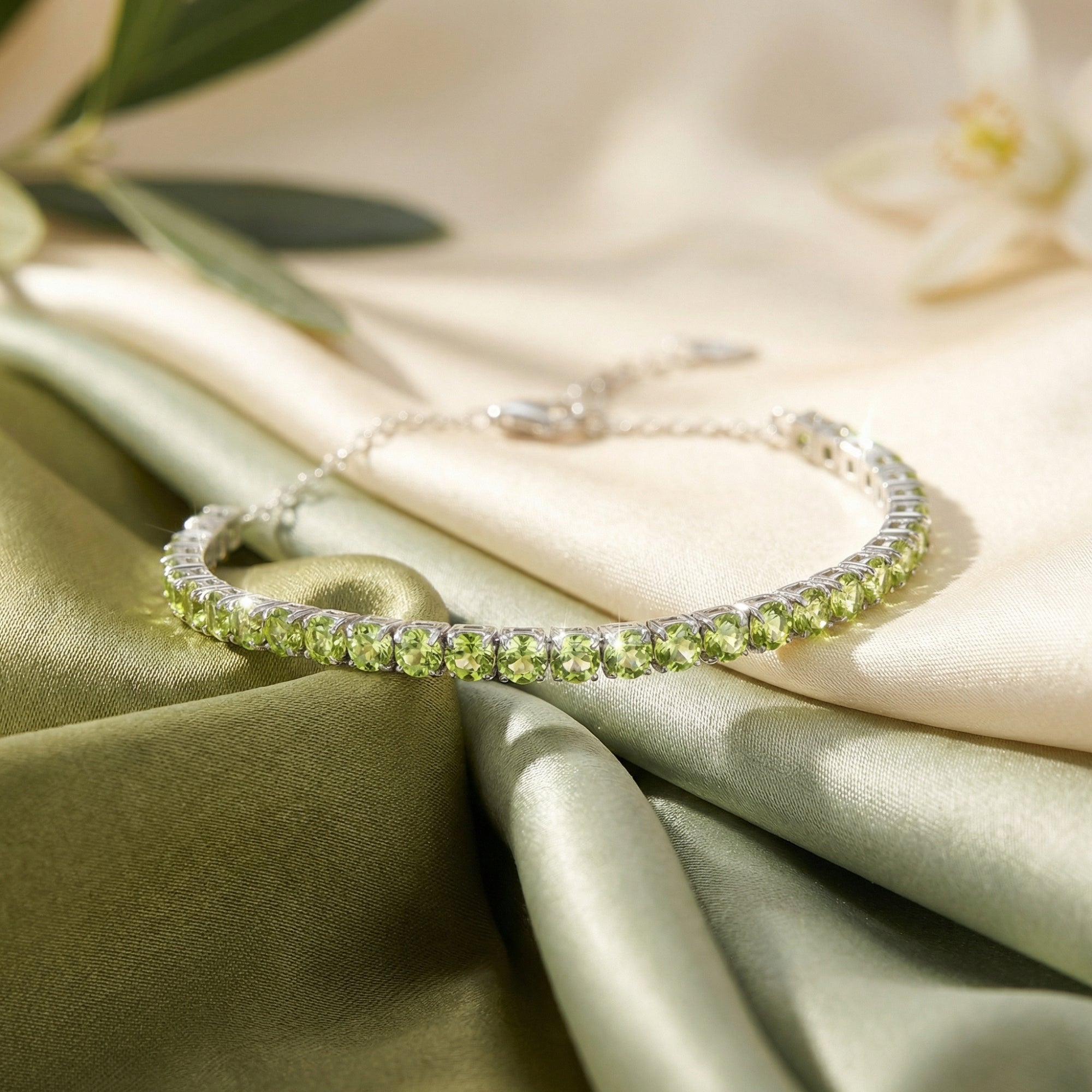 Round cut natural peridot tennis bracelet in sterling silver displayed on green and cream silk fabric.