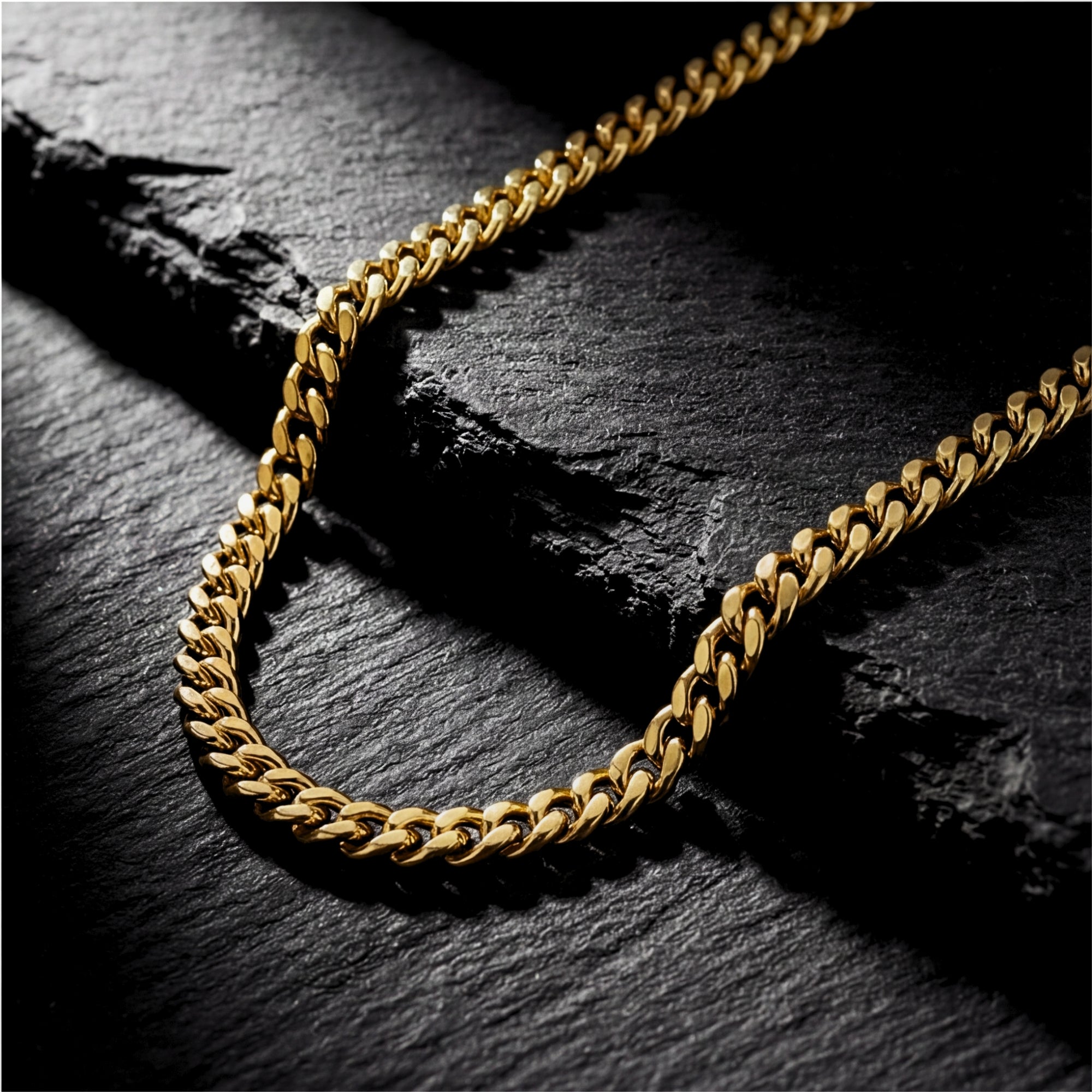4mm gold Cuban chain necklace in stainless steel draped over a dark textured stone background.