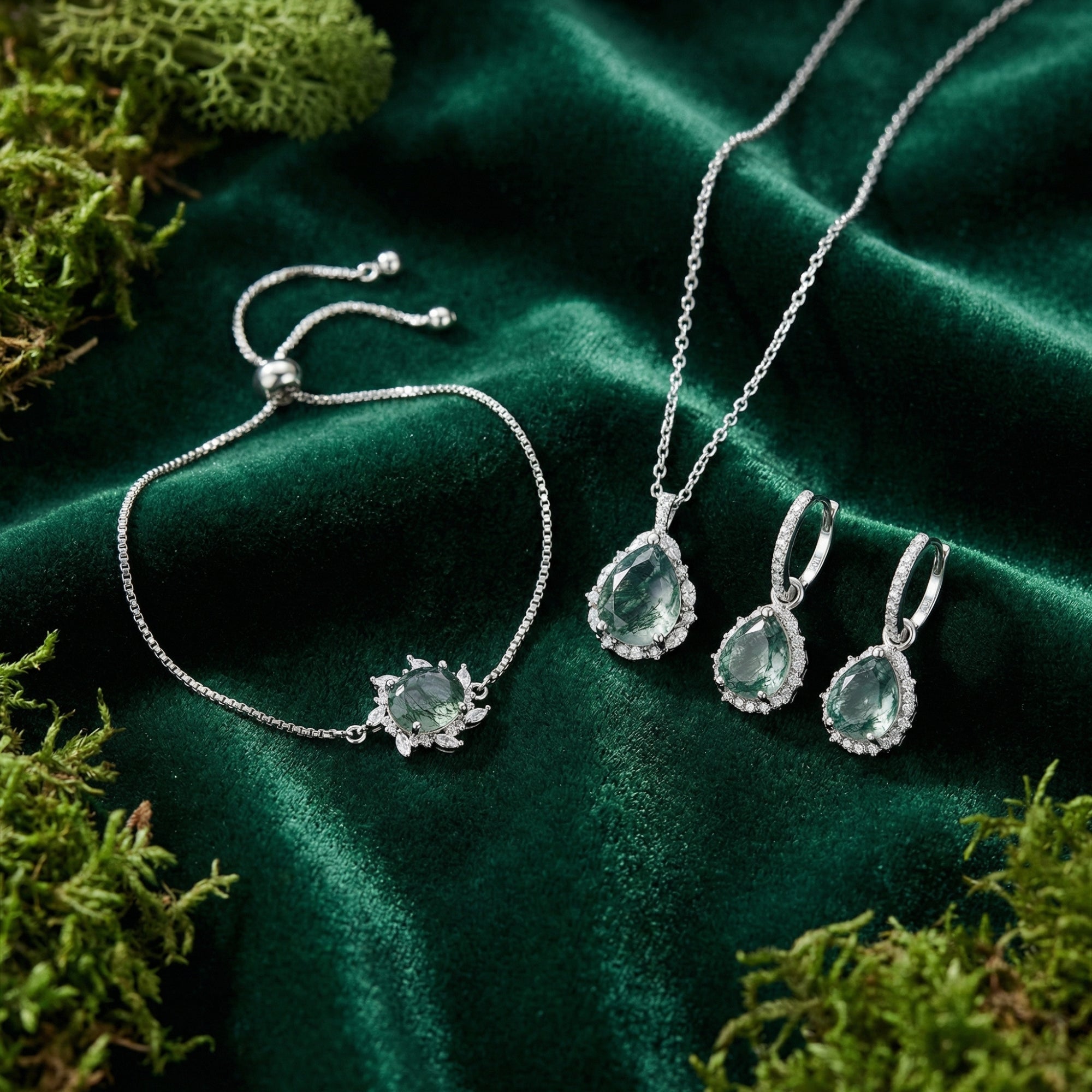 Moss Agate jewelry set with pear-cut necklace, earrings, and bracelet on green velvet with forest moss.