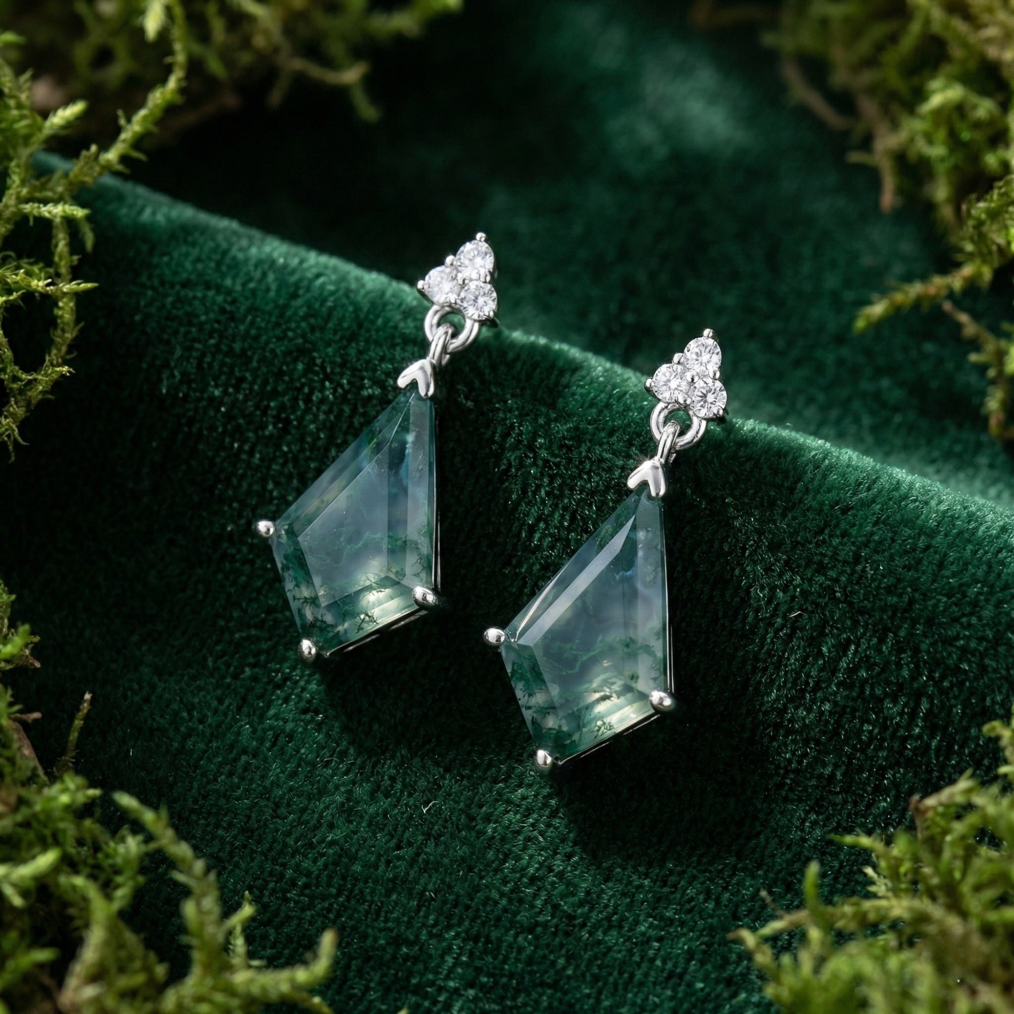 Kite cut moss agate drop earrings in sterling silver resting on green velvet surrounded by natural moss.