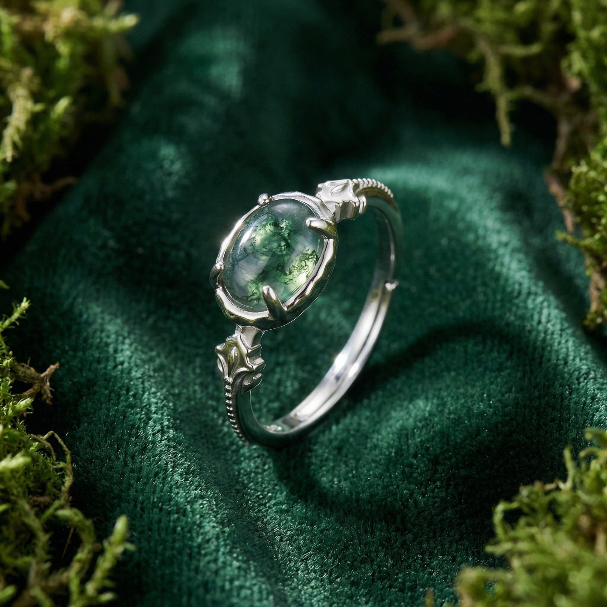 Oval natural moss agate ring in S925 sterling silver with leaf engravings on a green mossy background.
