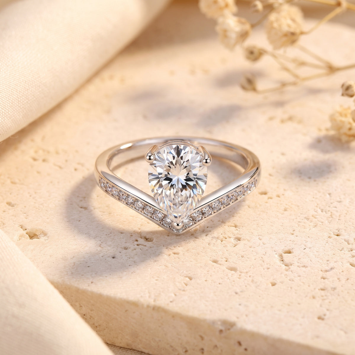 Silver chevron ring with a pear-shaped clear center stone and pave accents, displayed on a textured stone surface.