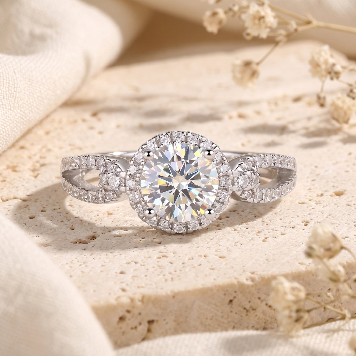 Front view of a silver halo ring with a round center stone and pavé infinity twist band on a beige stone surface.