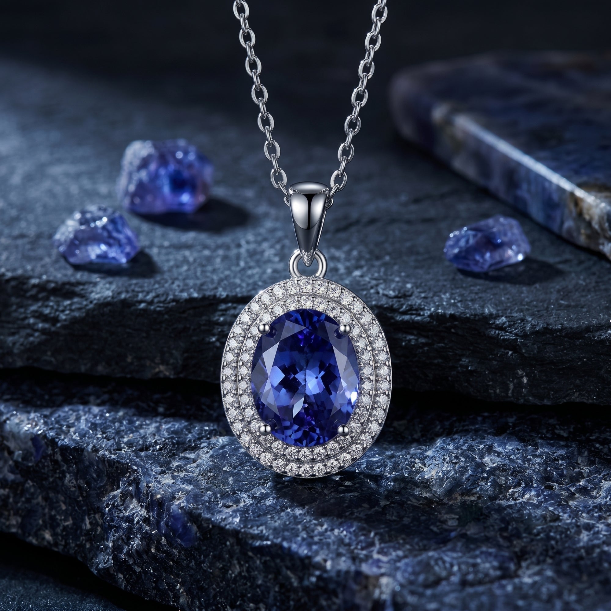 Oval tanzanite necklace in sterling silver with a double zircon halo, displayed on dark natural stones.