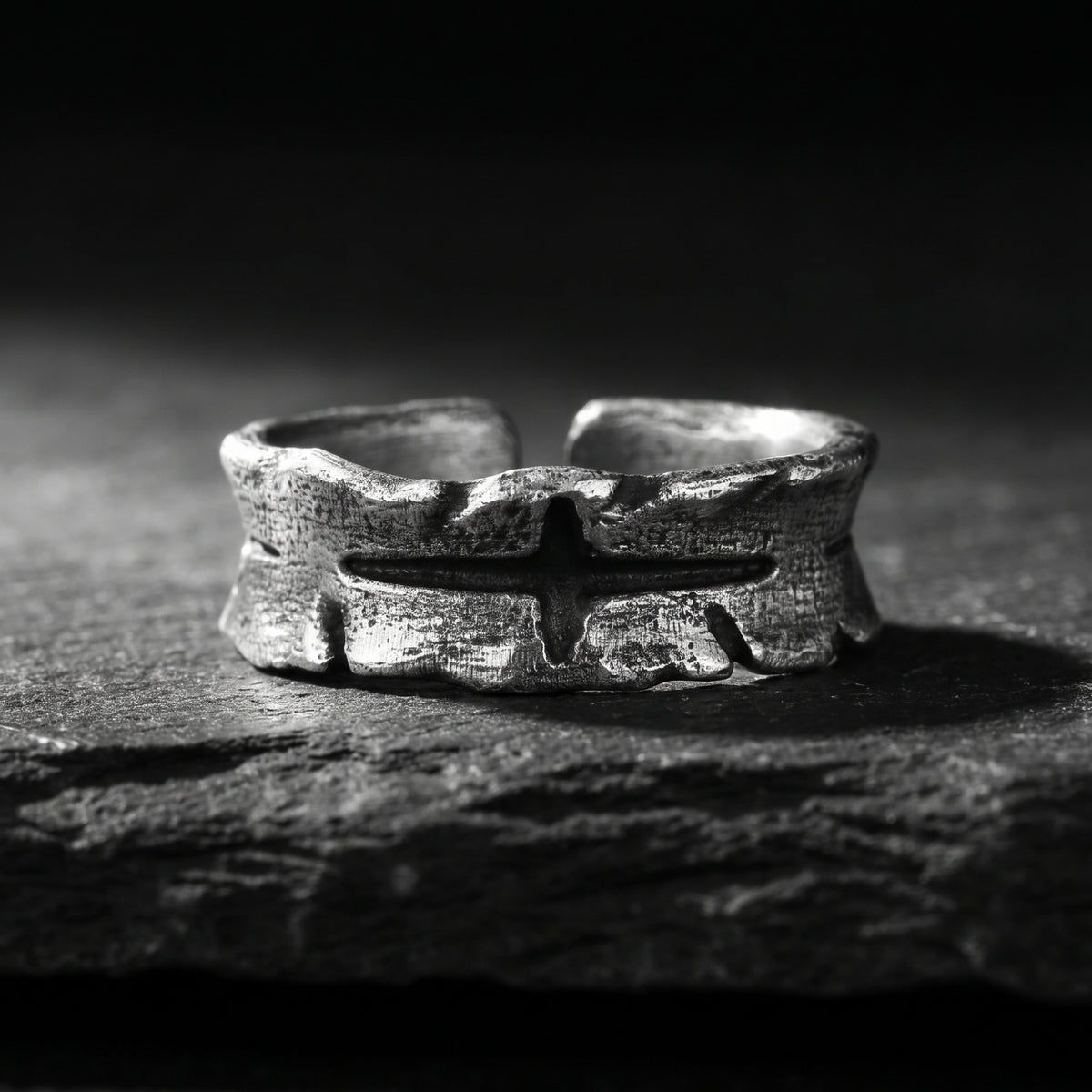 Front view of an open silver band ring with a bark-textured surface and carved central cross.