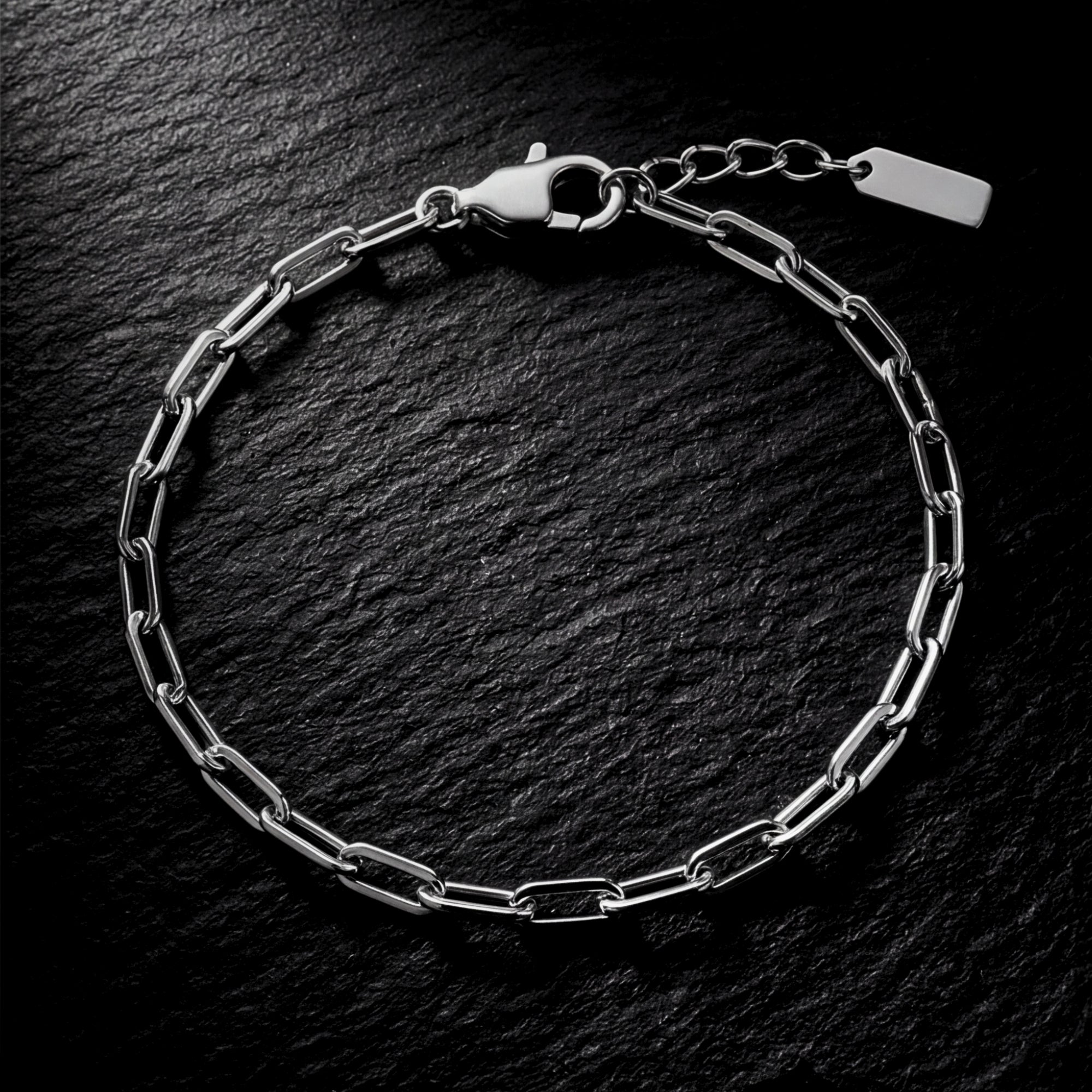 Silver stainless steel clip chain bracelet laid flat on a dark, textured stone background.