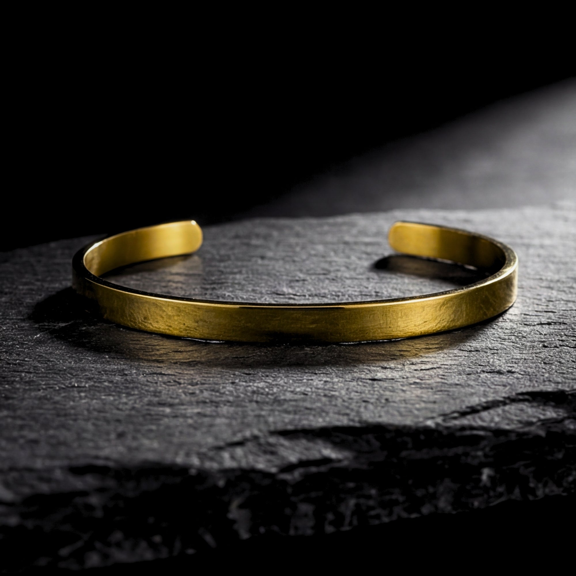 Classic gold stainless steel cuff bracelet for men resting on a dark textured stone surface.