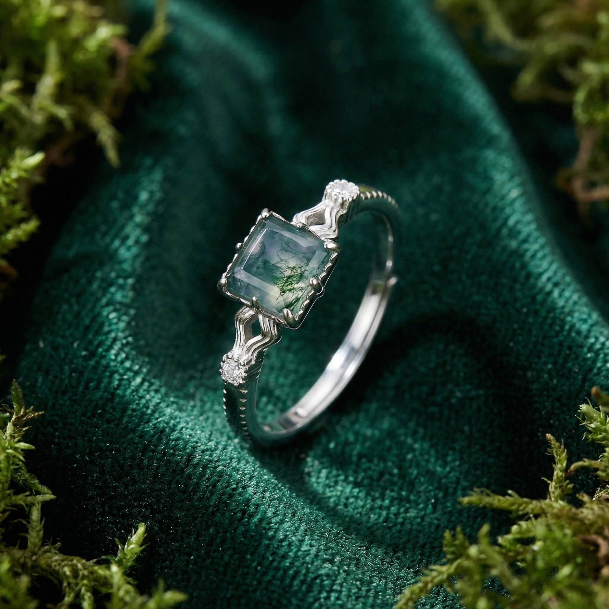 Cushion cut moss agate ring in S925 sterling silver with a wavy band, displayed on green moss and velvet.